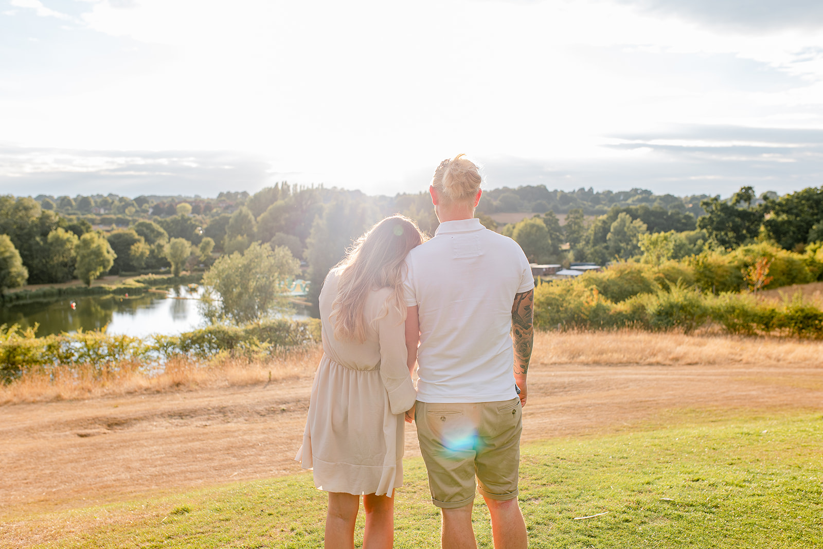 A couple standing side by side hugging each other, overlooking a lake at golden hour. 