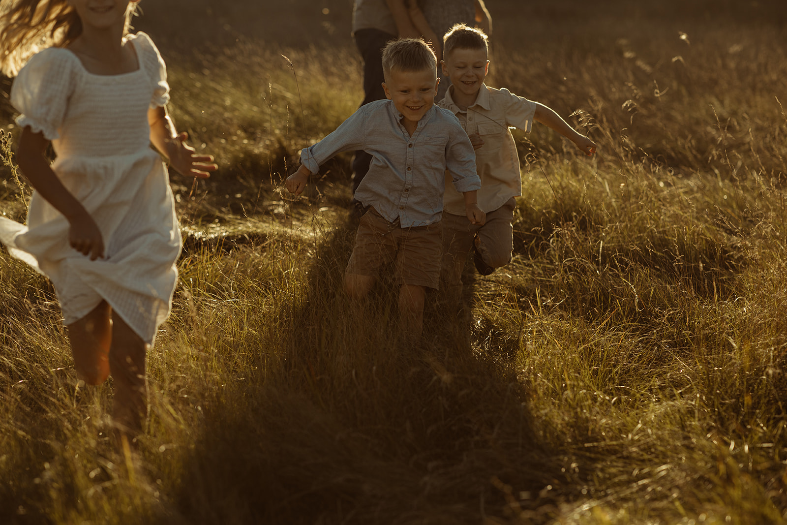 Children running through a field at sunset