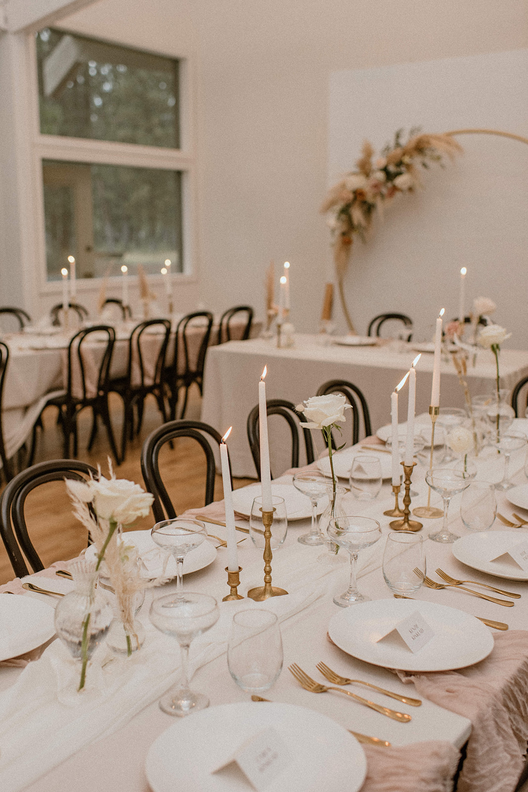 Elegant long dinner table for a white wedding with black bentwood chairs and gold taper candles