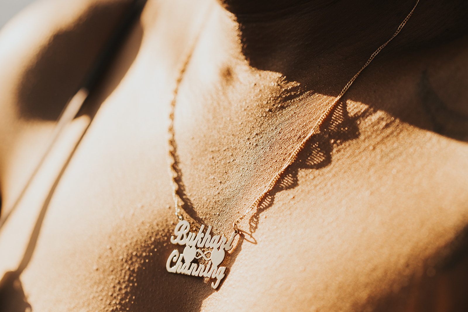 Close up shot of golden necklace with Channing and Bukhari's names against goosebump skin. 