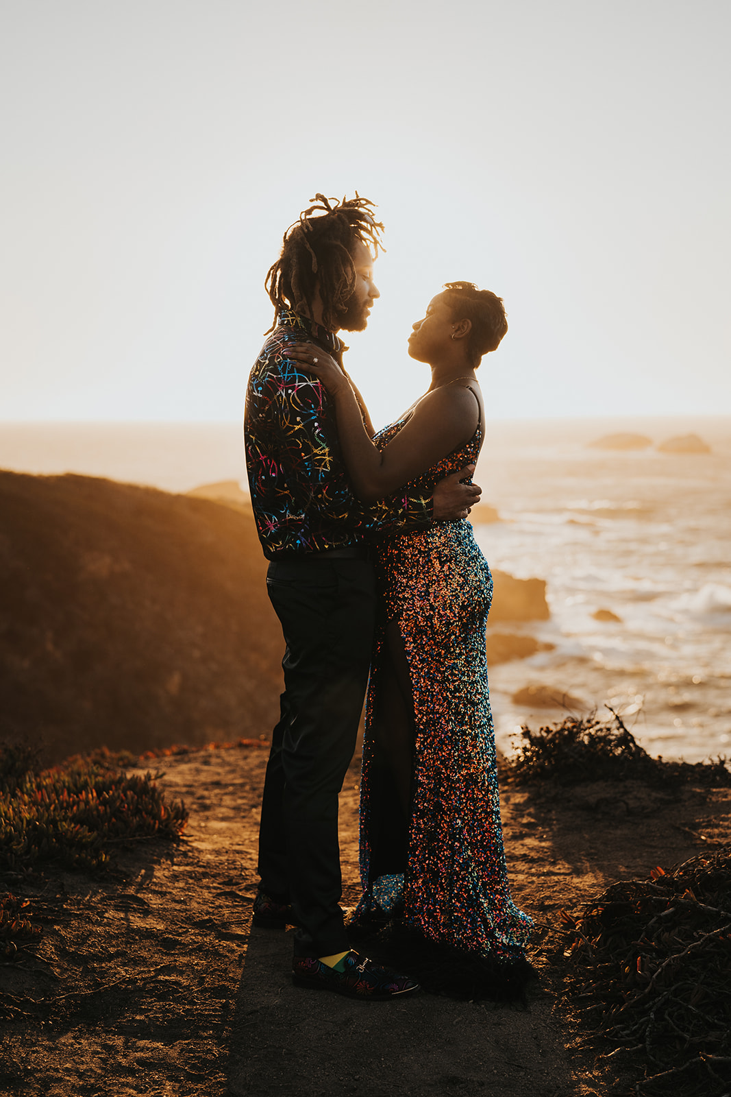 Couple stands facing each other in embrace backlit by the sun