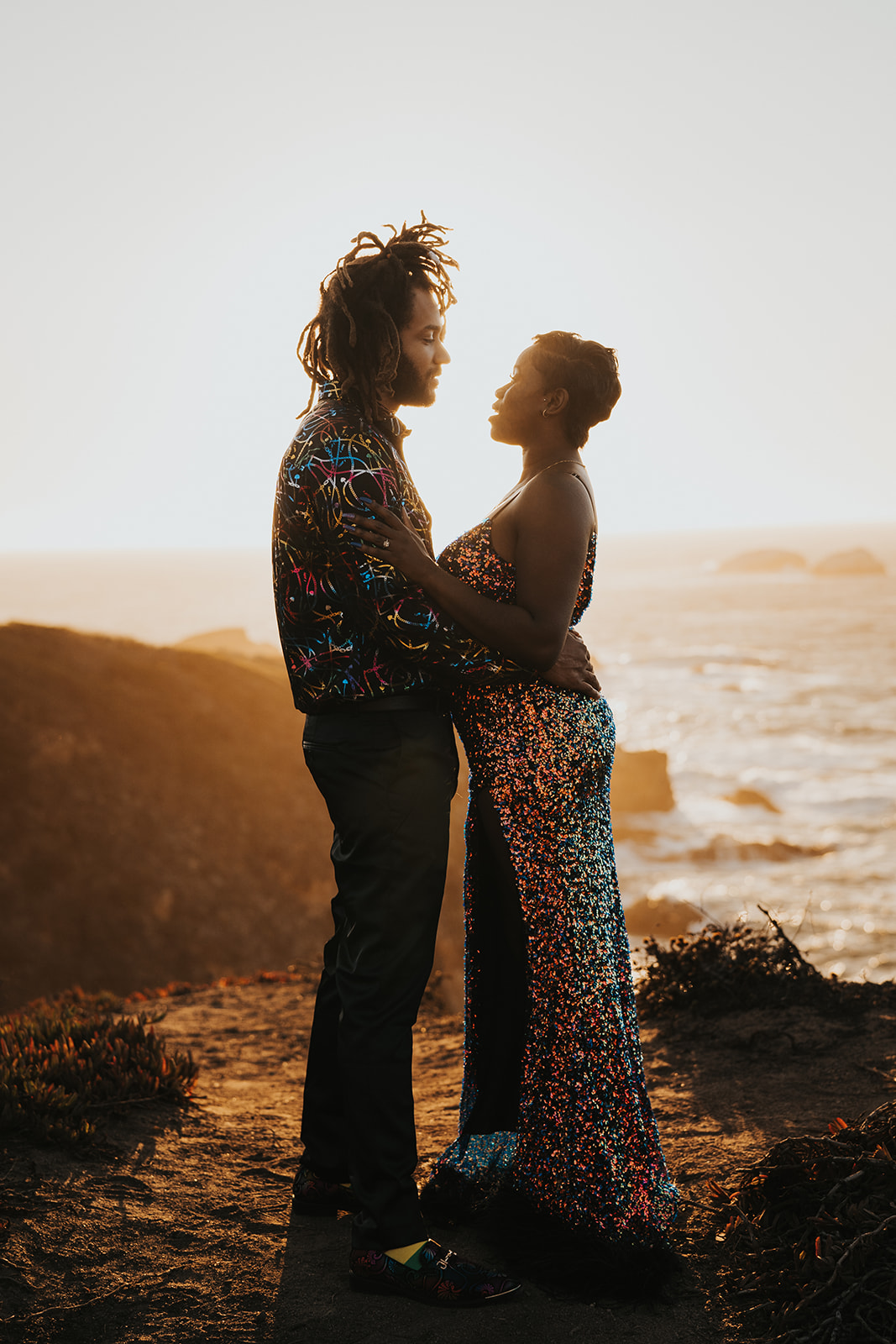 Couple stands facing each other in embrace backlit by the sun