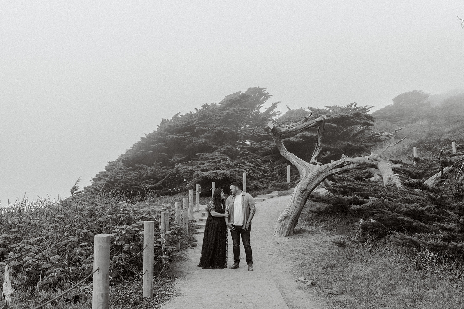 Black and white of a couple celebrating their engagement in the fog at Lands End San Francisco CA