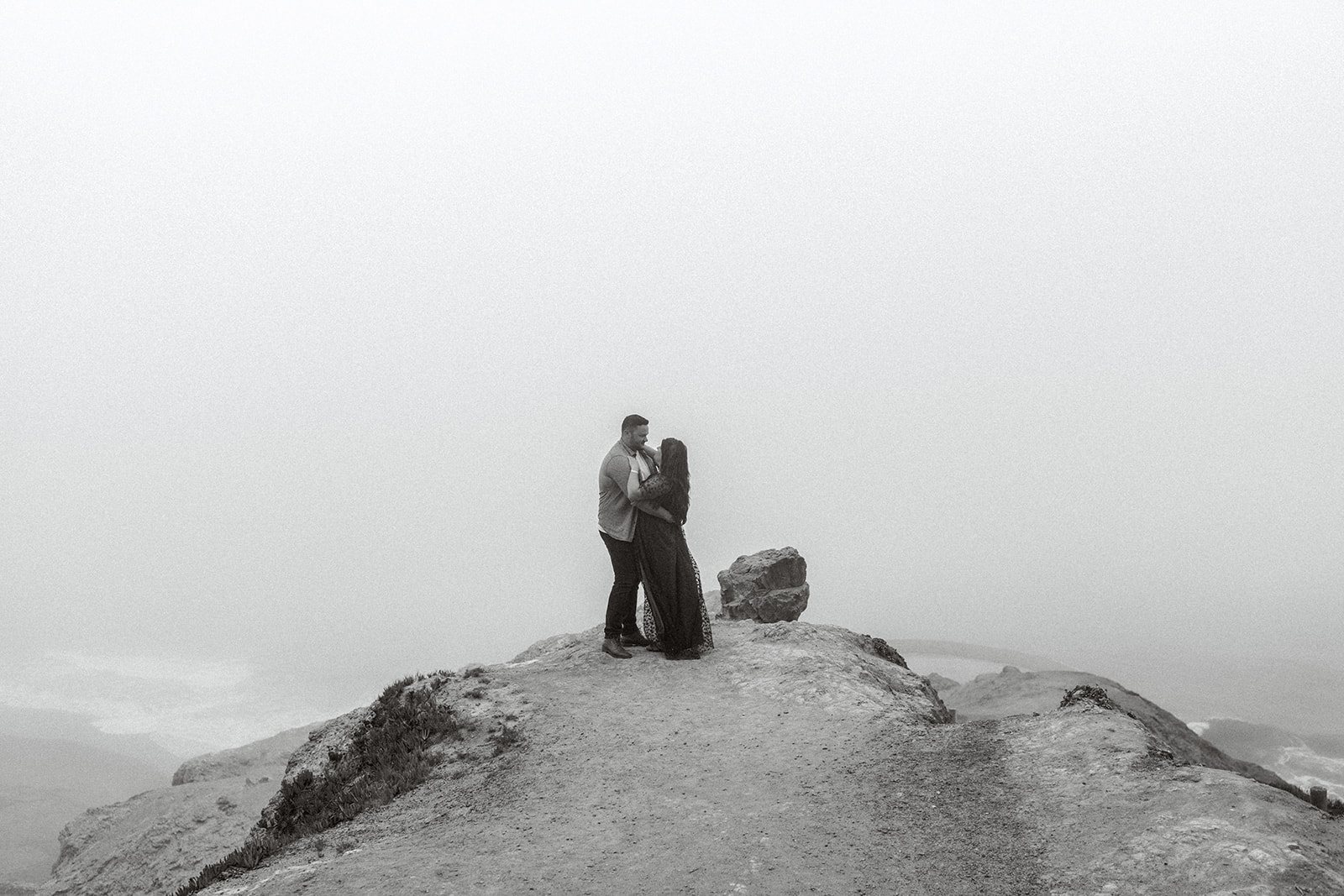 A couple celebrates their engagement at the beach in the fog at Lands End San Francisco, CA.
