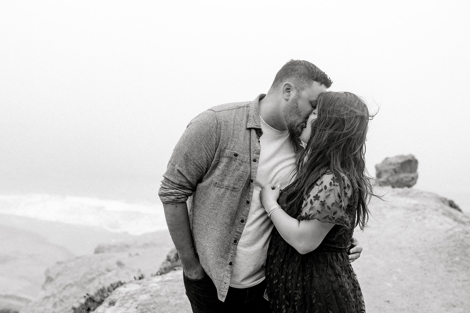 A couple celebrates their engagement at the beach in the fog at Lands End San Francisco, CA.