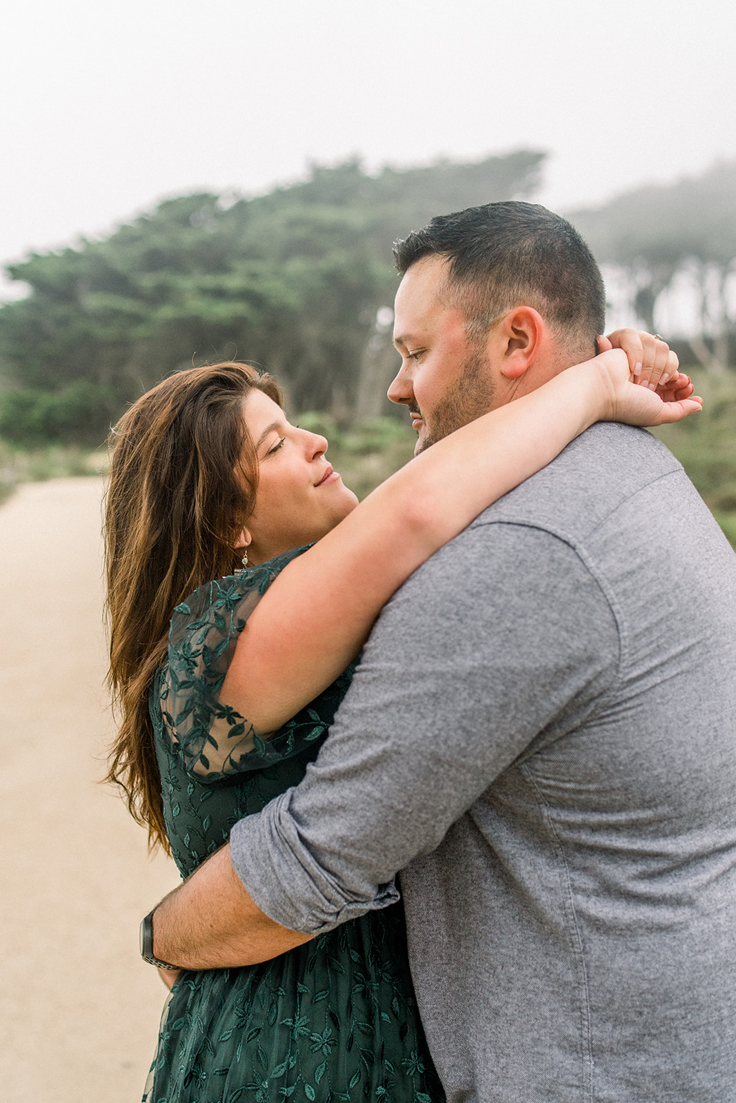 A couple celebrates their engagement in the Cypress trees in fog at Lands End San Francisco CA.