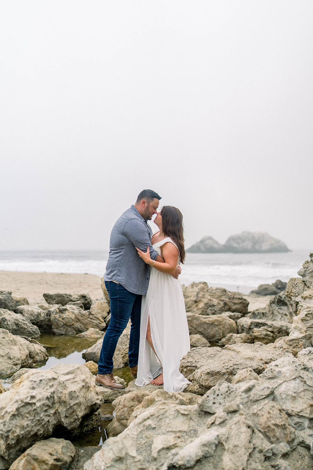 A couple celebrates their engagement in the Cypress trees in fog at Lands End San Francisco, CA.