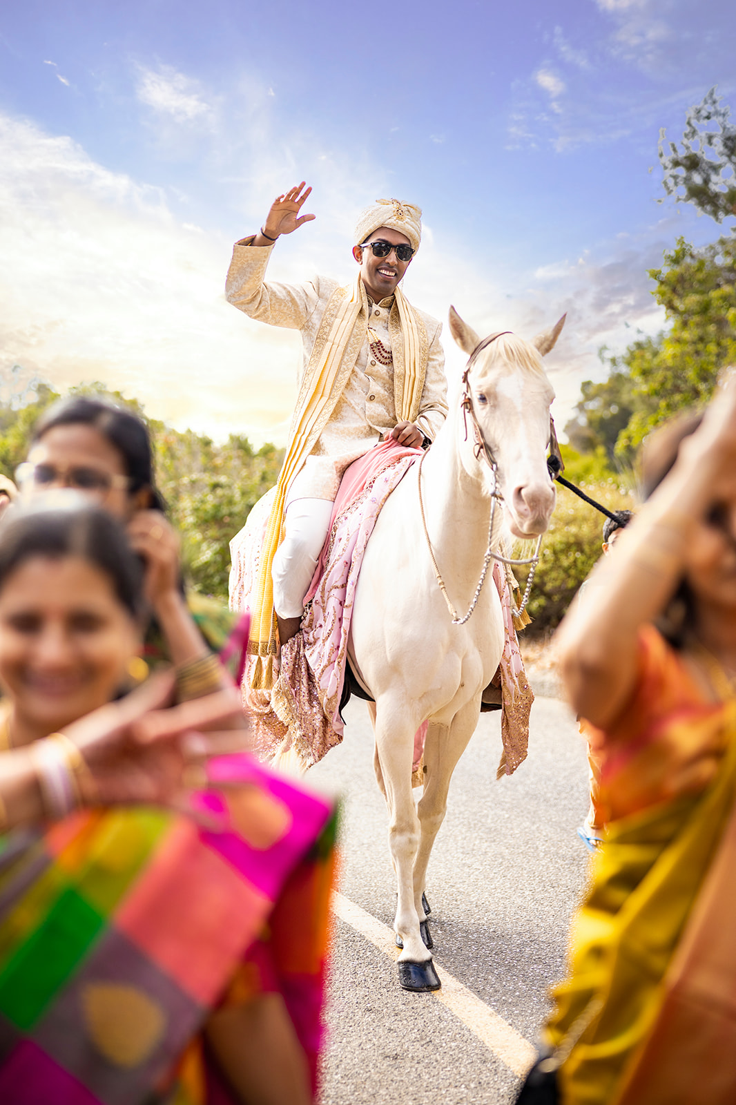 Indian groom waives to onlookers and family in the bay area at his wedding while on top of a horse.