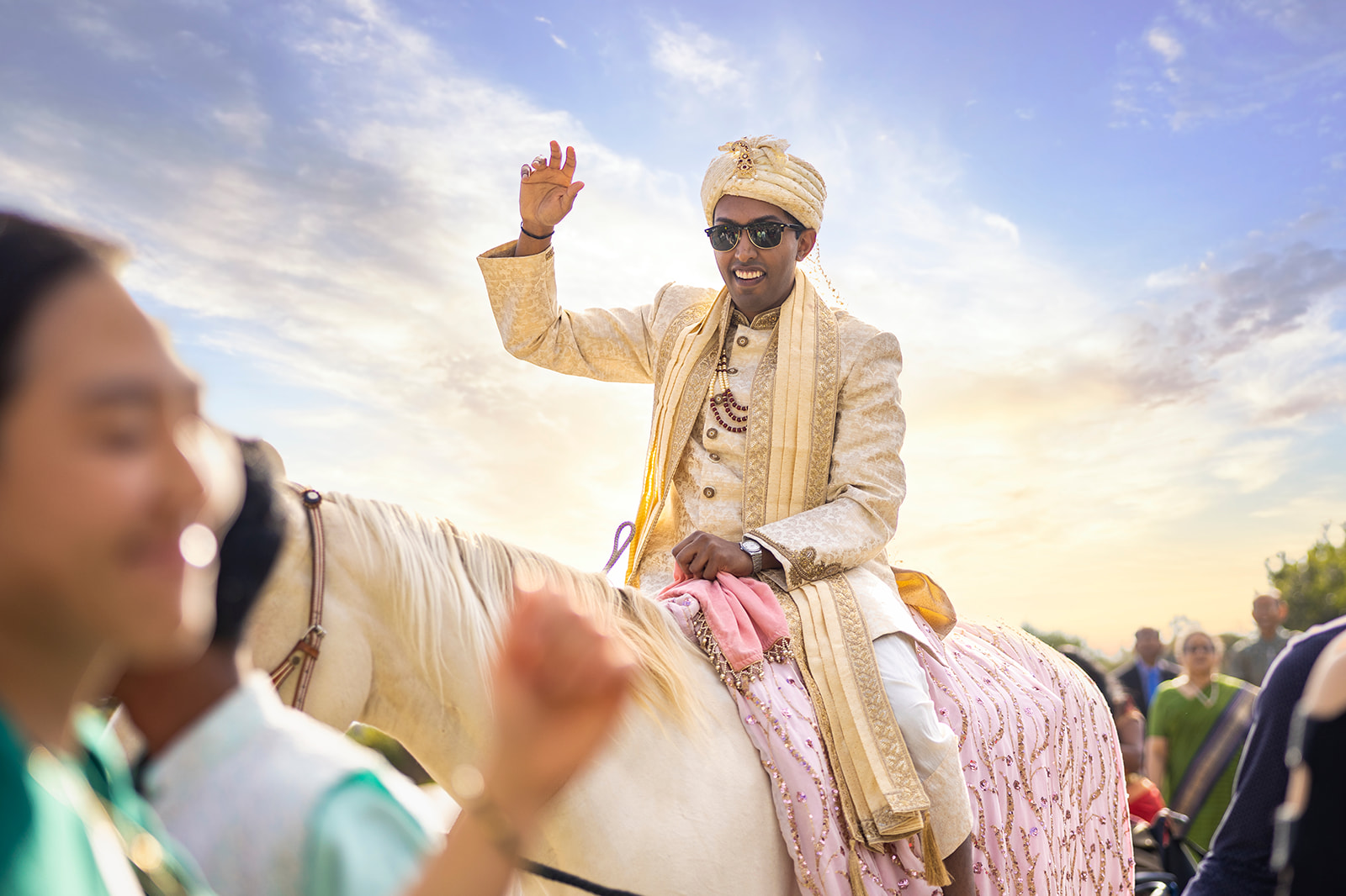 Indian groom waives to onlookers on top of a horse during barat at Renstorff House.