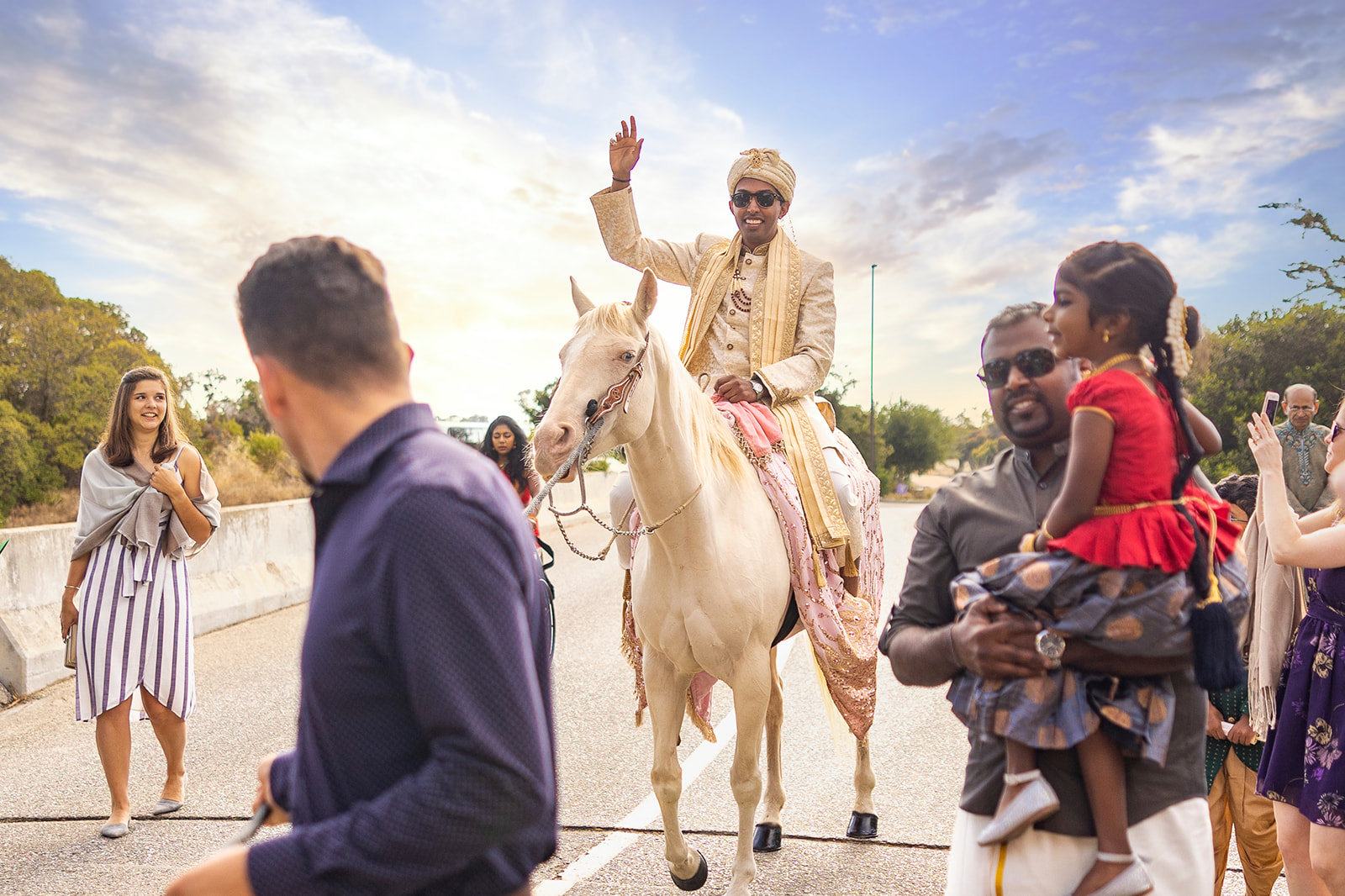 While riding a horse, Indian groom waives to spectators at Indian wedding.
