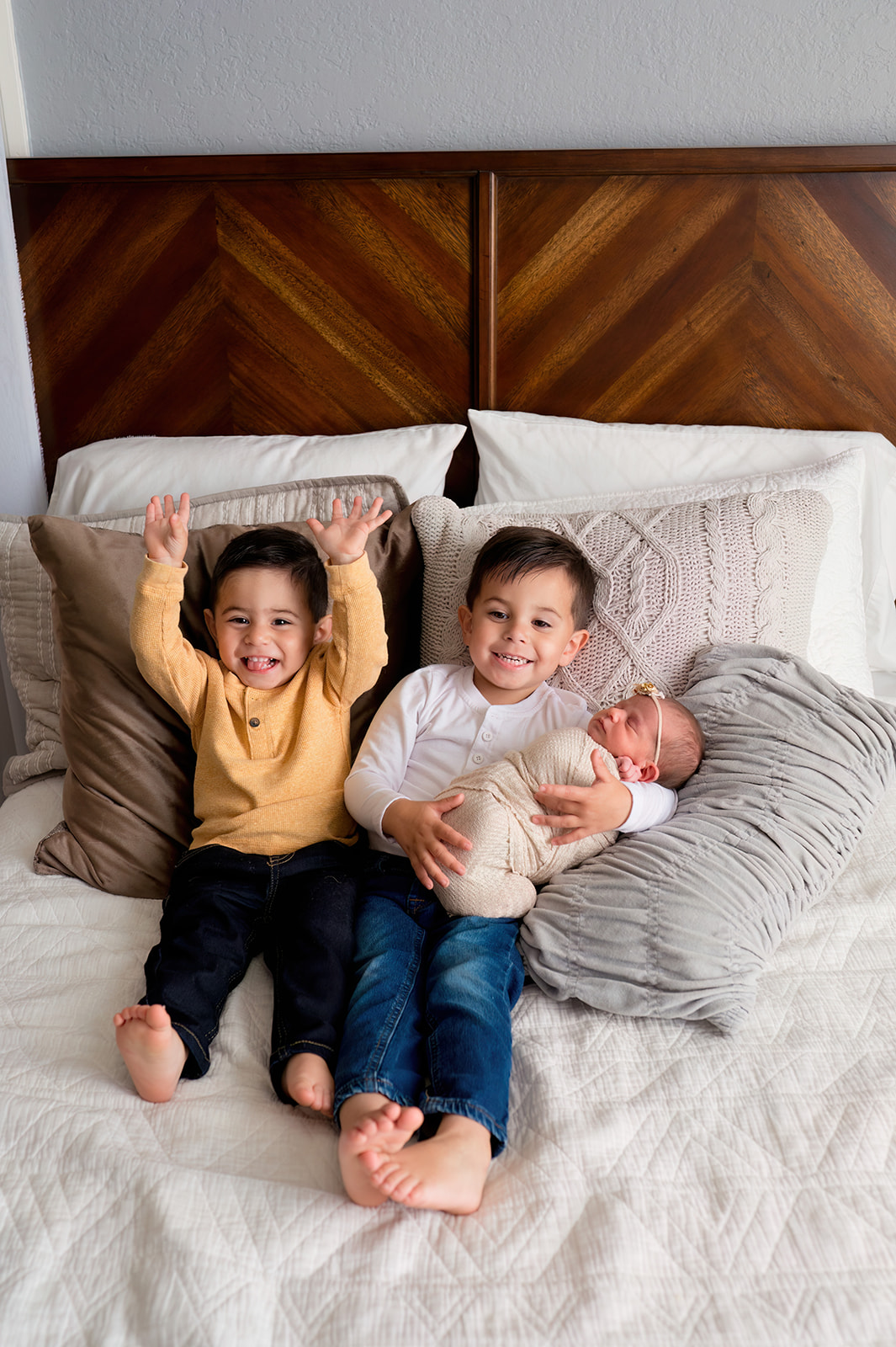 Proud big brothers hold newborn baby girl in bedroom set of loveland photography studio