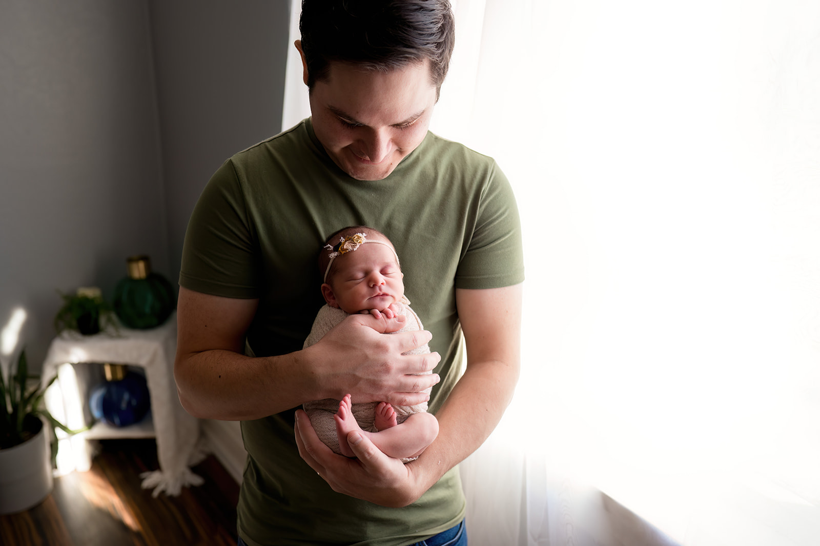 Proud father holding newborn baby girl swaddled in pink by window in downtown loveland