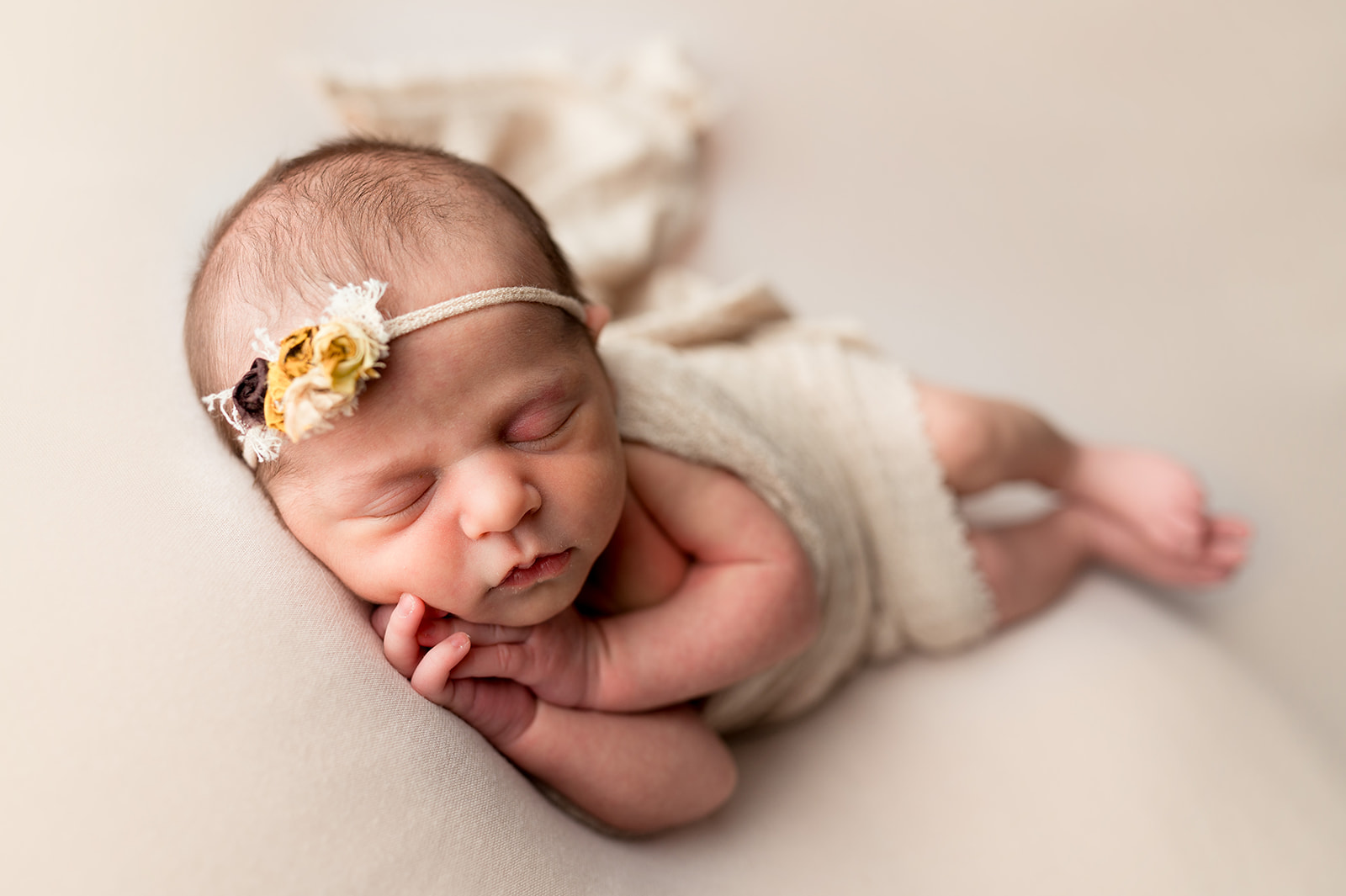 Side lying baby girl with hands tucked under her cheek on a cream background with a yellow headband