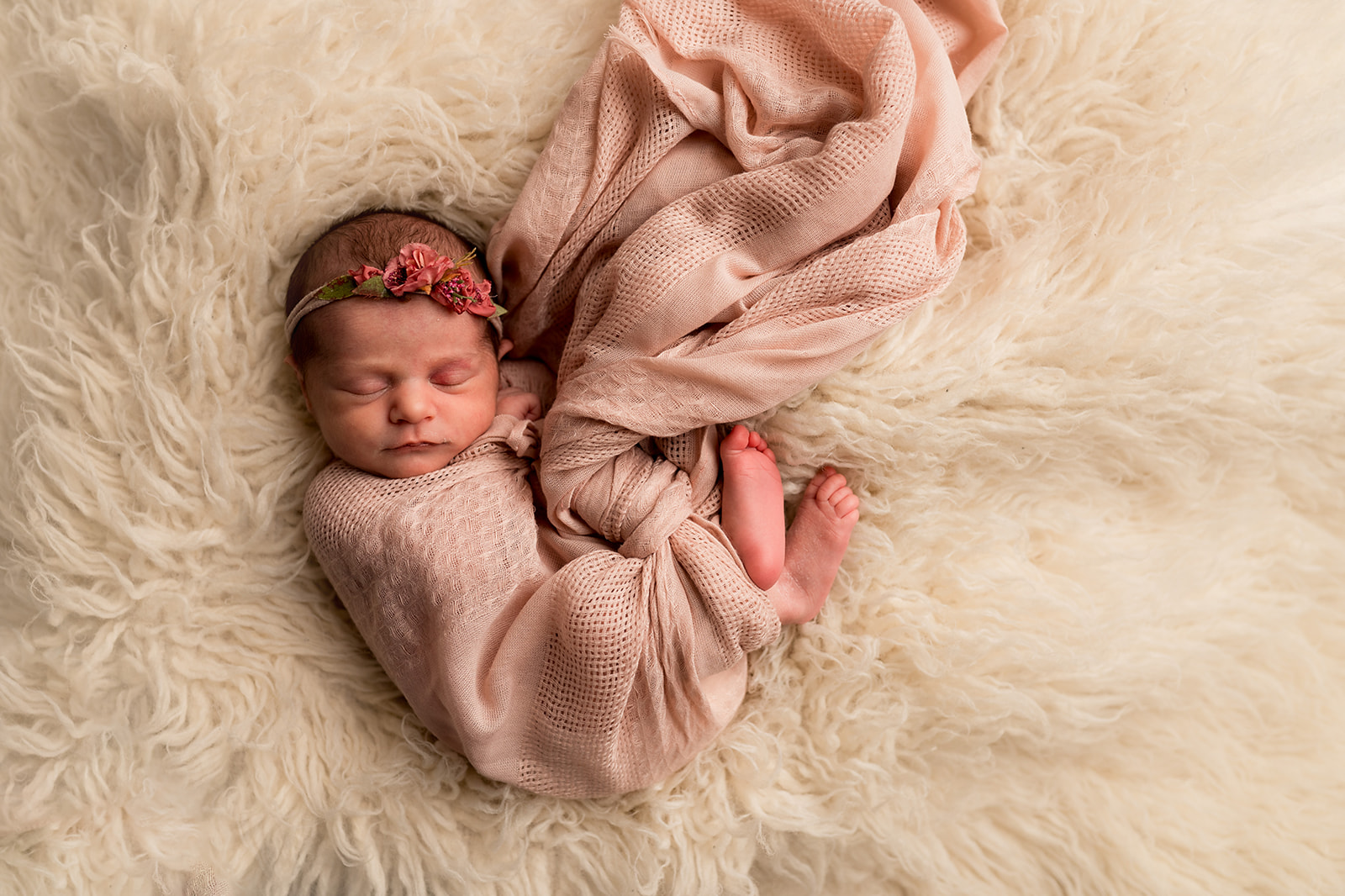 swaddled baby girl in pink on cream fur rug sleeping for newborn session
