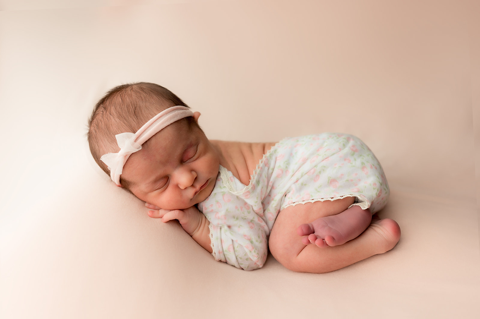tushy up pose of newborn baby girl on pink backdrop with floral onesie and pink bow