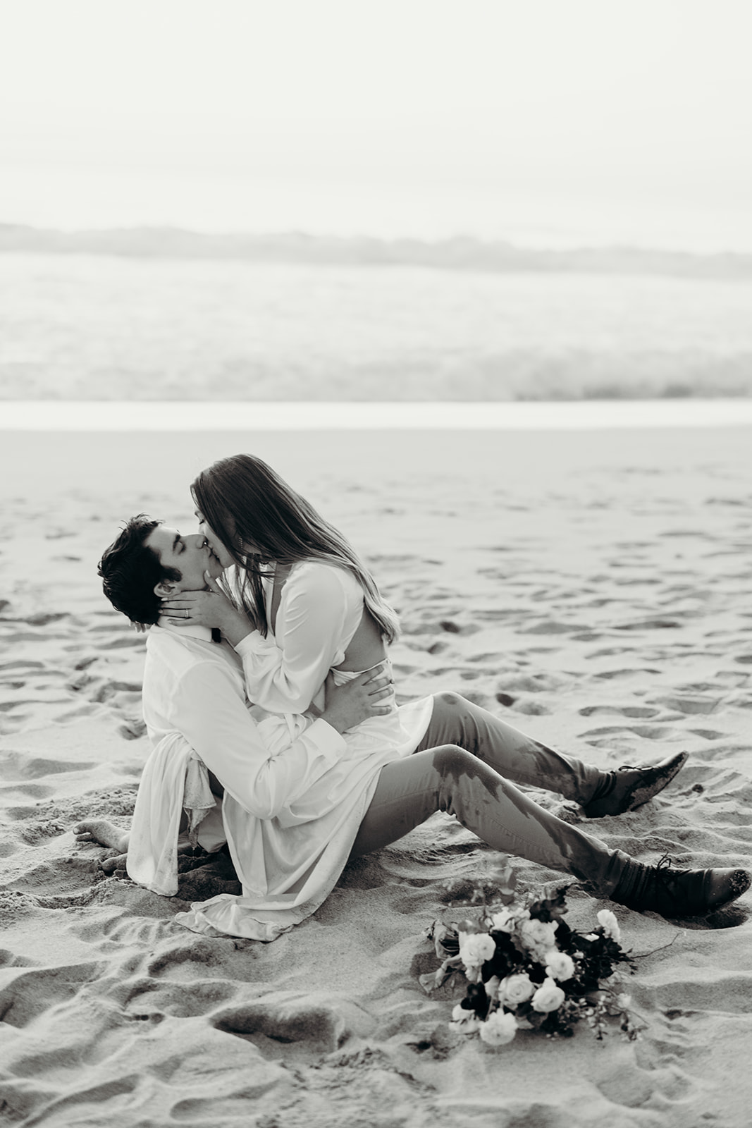 a black and white photo of a couple kissing in the sand
