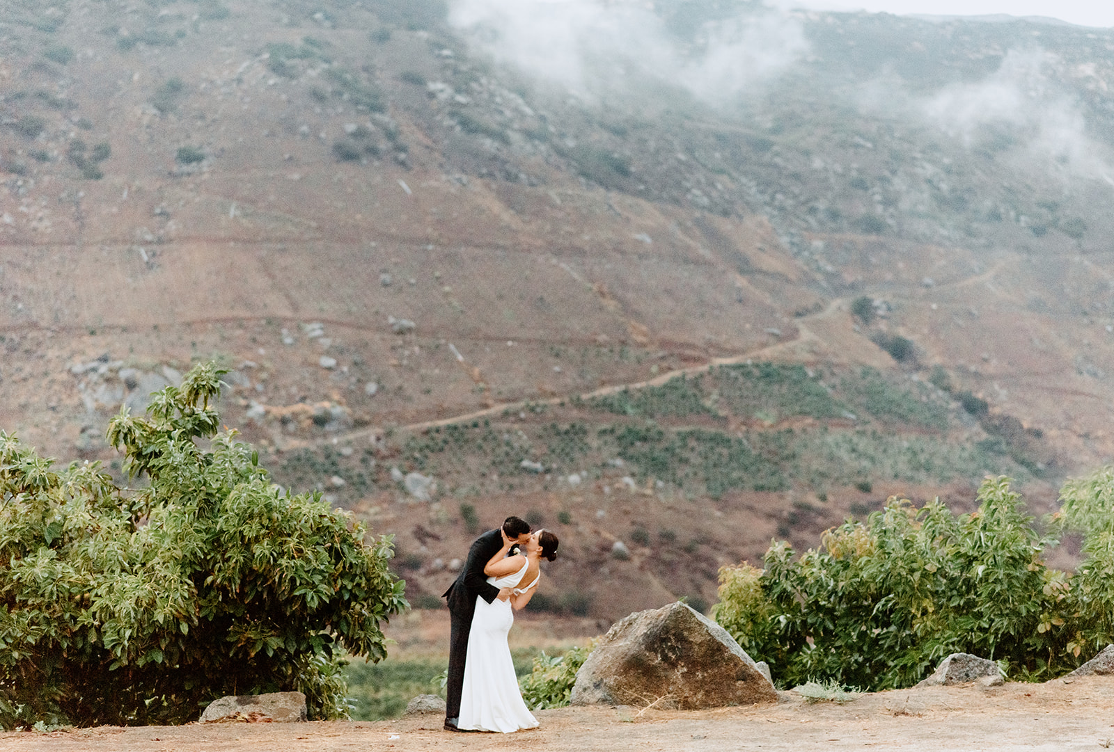 Couple taking portraits with their wedding photographer, with their wedding venue, Rancho Guejito, in the background