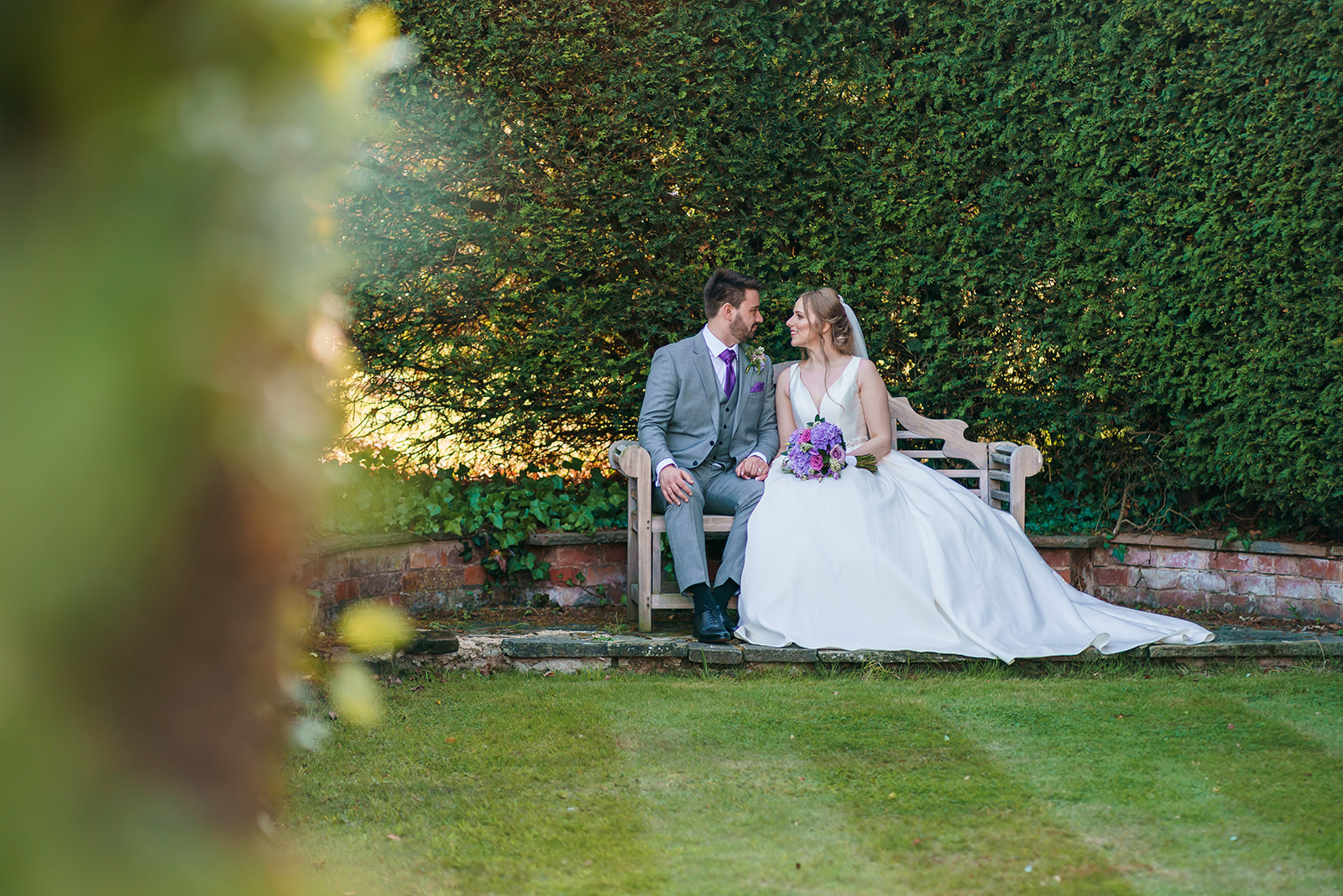 Bride and groom on a bench in Bourton Hall gardens