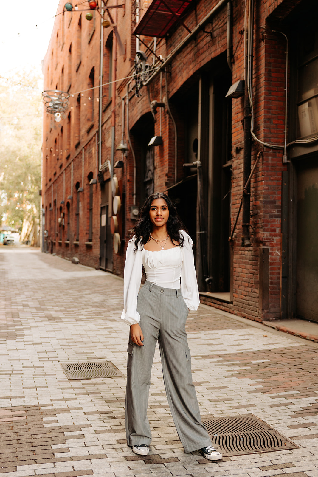 An edgy photo of an ethnic high school senior girl posing in front of a brick alleyway in Pioneer Square, Seattle.