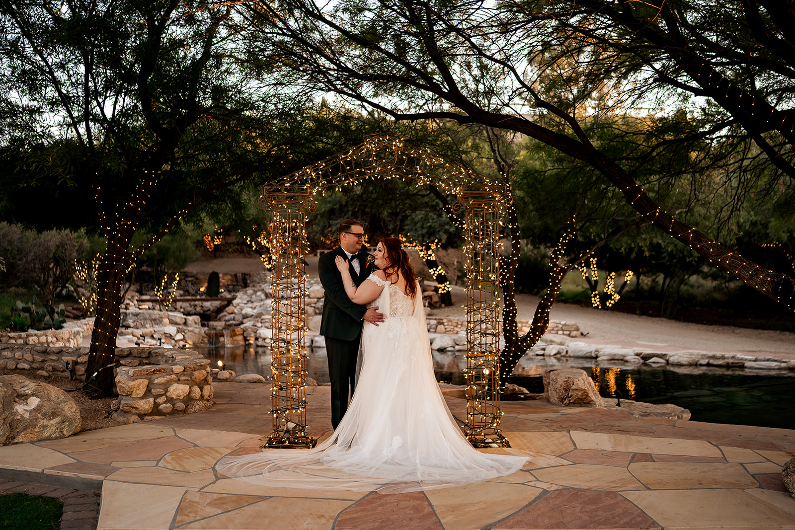 wedding couple hugging under twinkle lights arch at saguaro buttes wedding venue