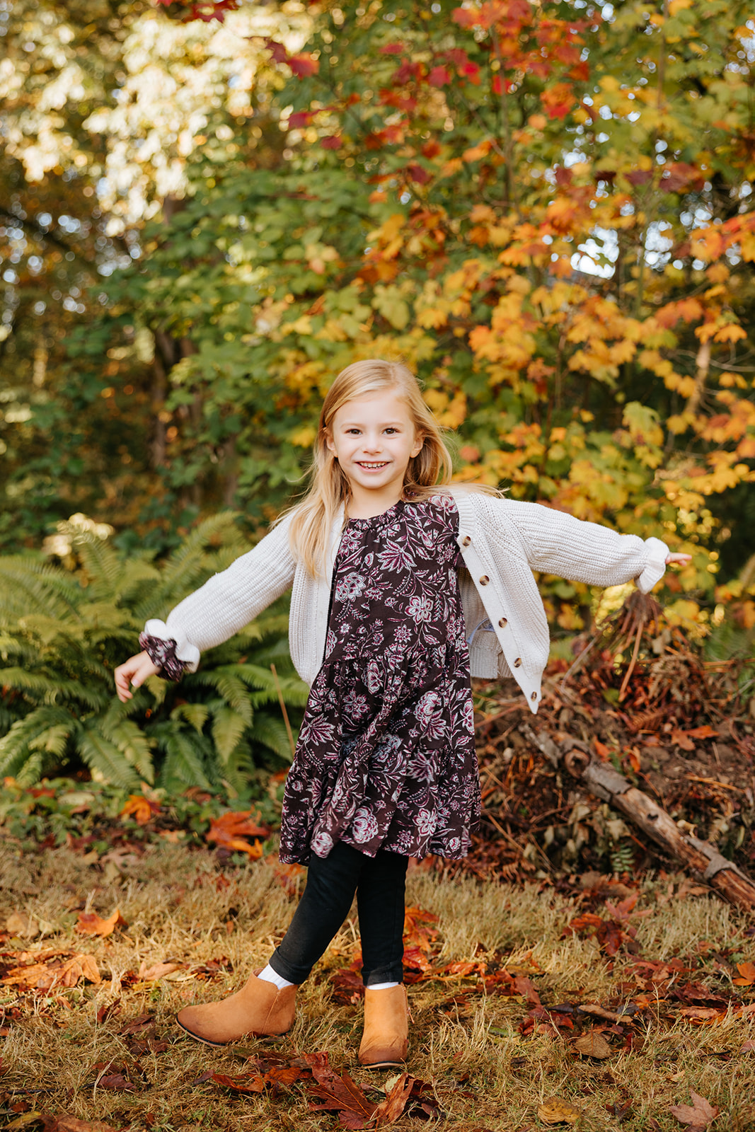 A young girl twirling at a park while smiling at the camera in the fall.