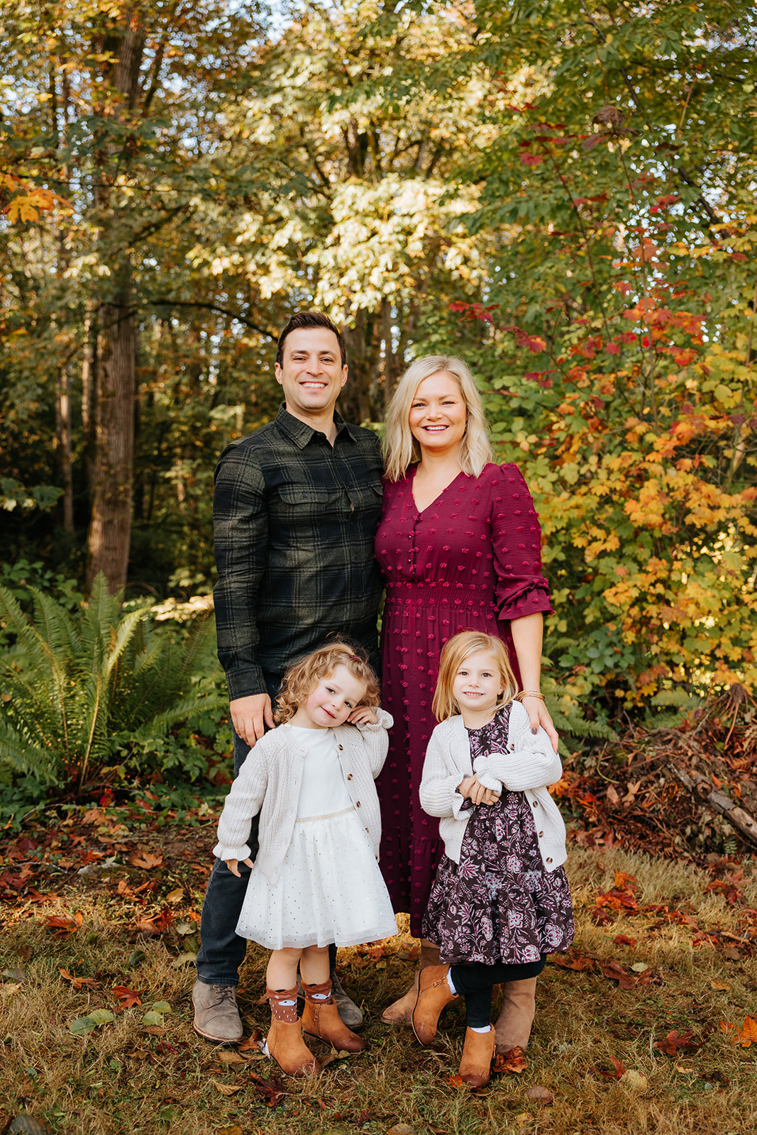 A photo of a happy family hugging each other and smiling at the camera in front of colorful fall foliage.