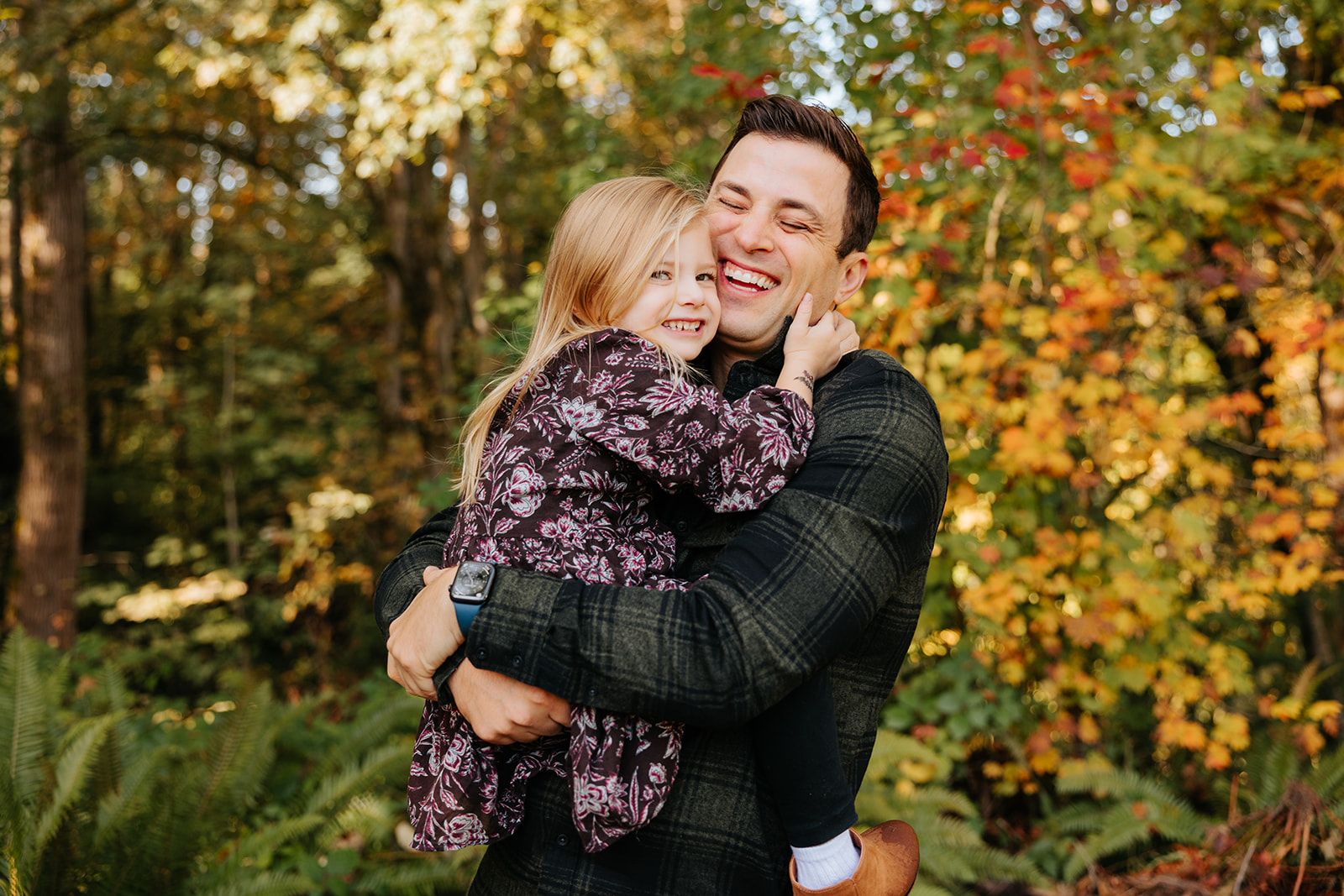 A close-up candid photo of a father holding his daughter in his arms in front of colorful fall foliage in Seattle.