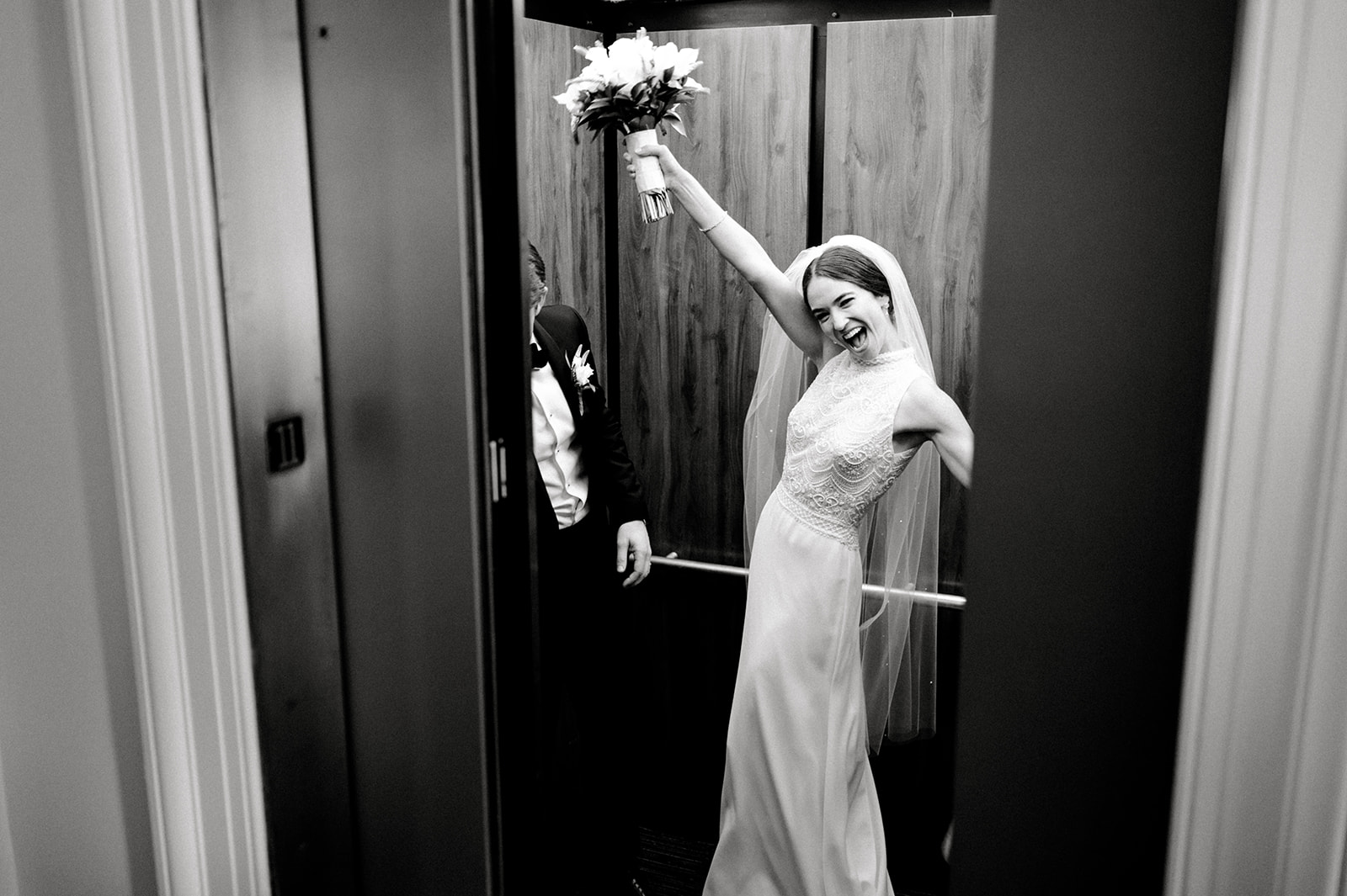 black and white post ceremony bride and groom taking the elevator solo, bride celebrating with flowers in the air.