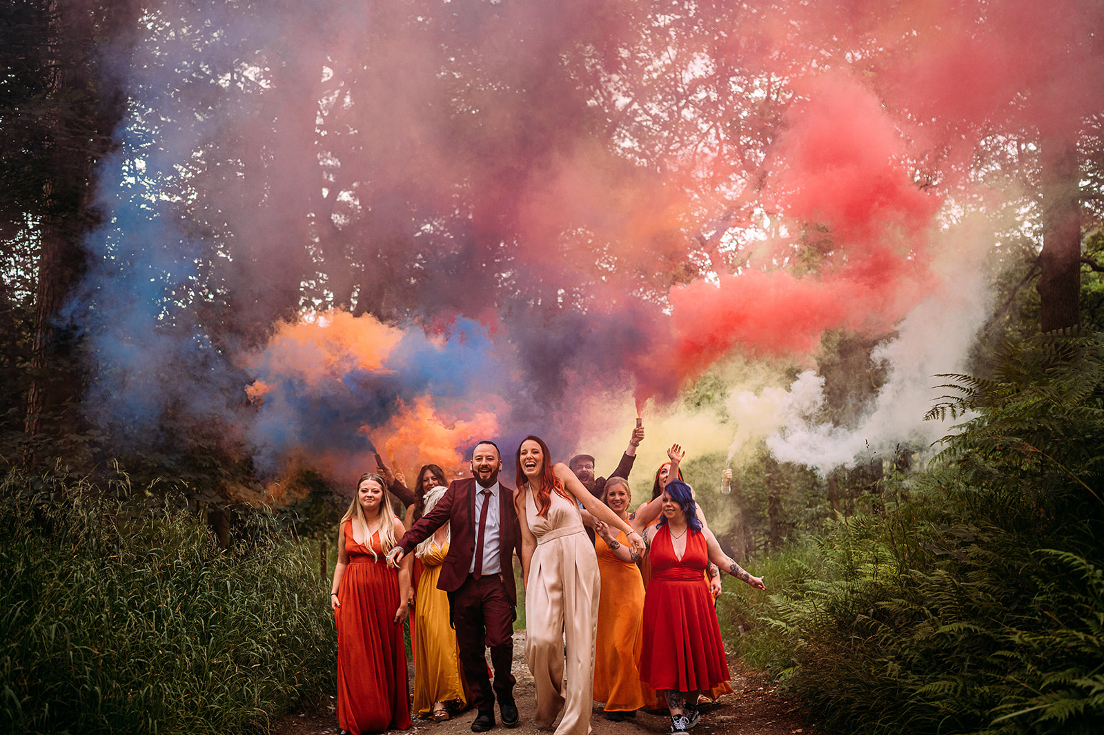 The wedding party walk through the woods with colourful smoke flares.
