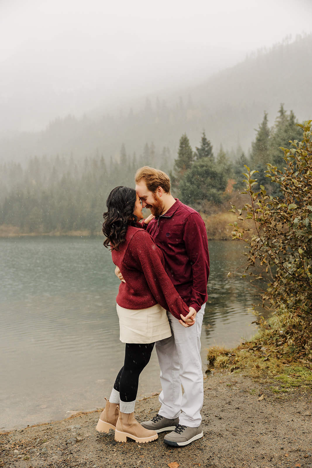 A photo of a loving couple holding hands near a winter pond in the mountains of Washington while the snow falls.