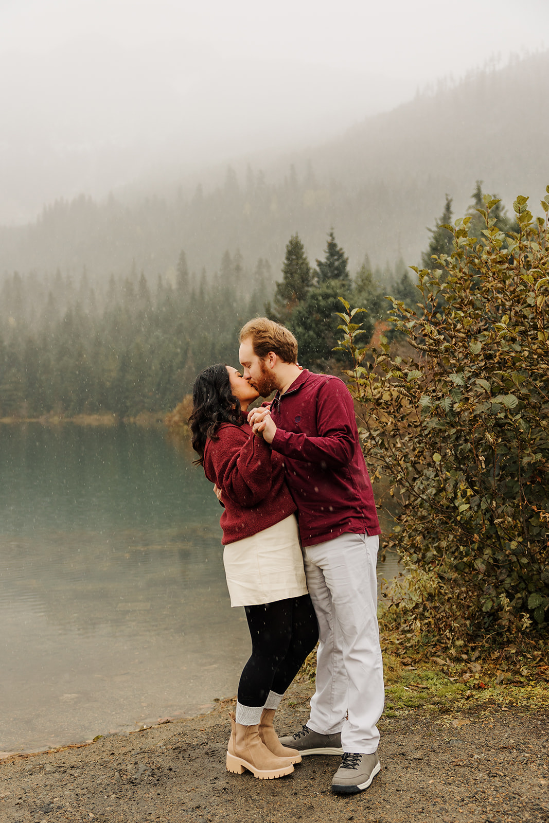 A photo of a loving couple kissing near a winter pond in the mountains of Washington while the snow falls.