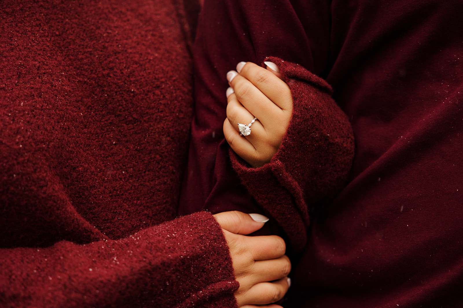 A close-up photo of a couple linking arms with a focus on the woman's engagement ring.