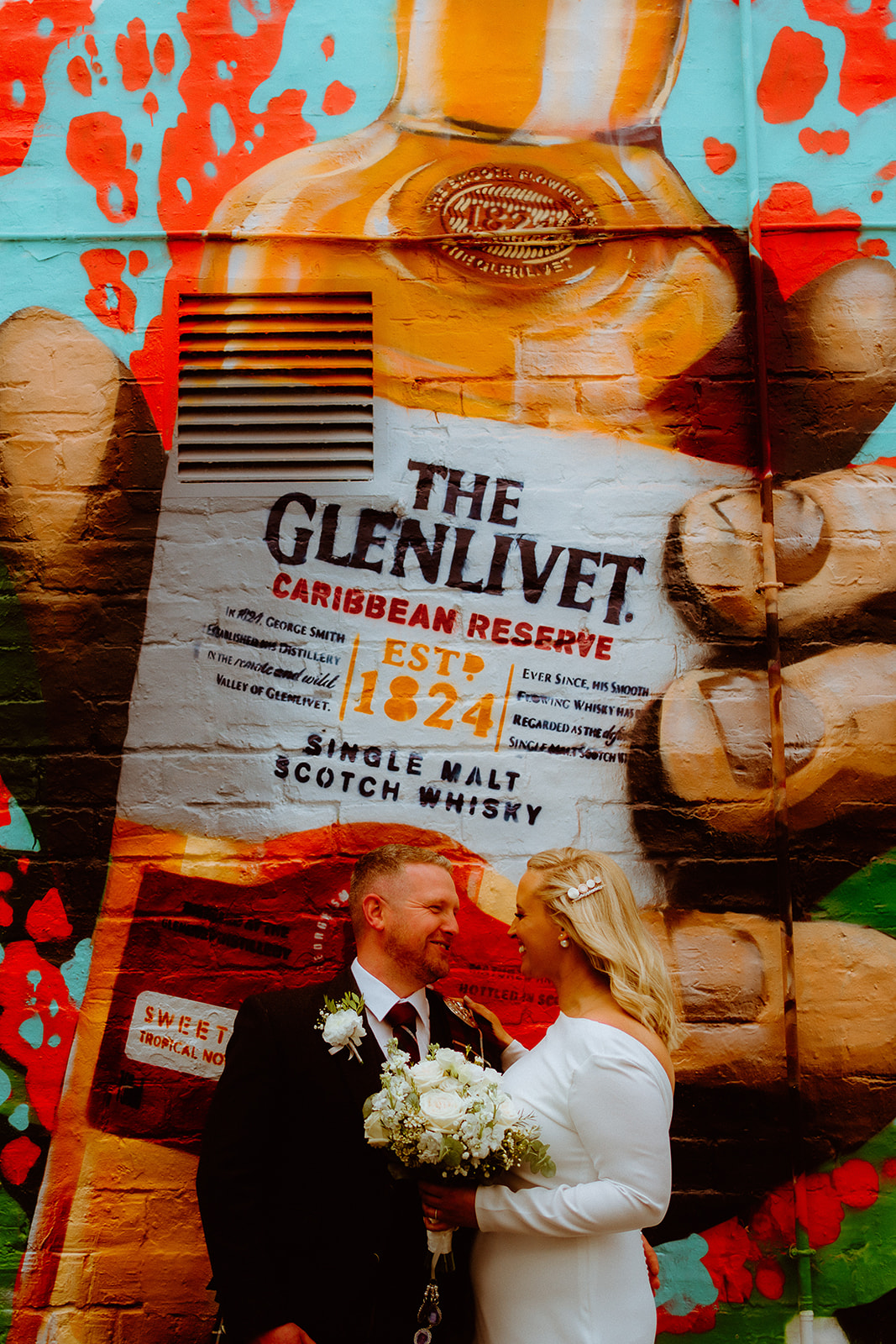 Wedding couple, standing in front of mural in Glasgow.