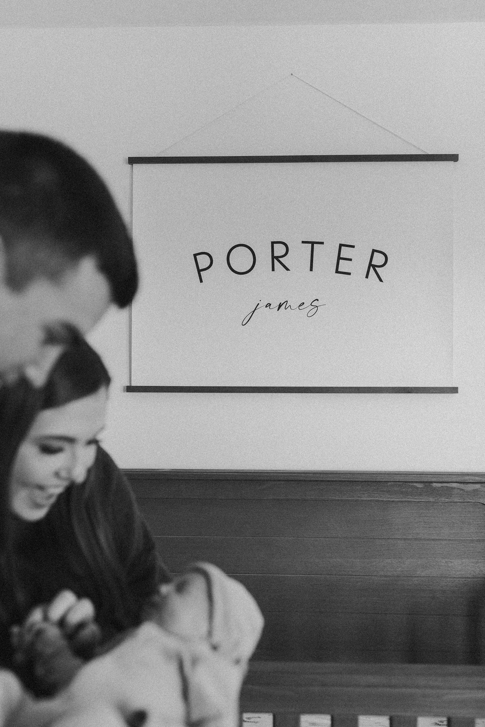 couple holding baby in nursery with name sign in background during in-home newborn family photo session. 