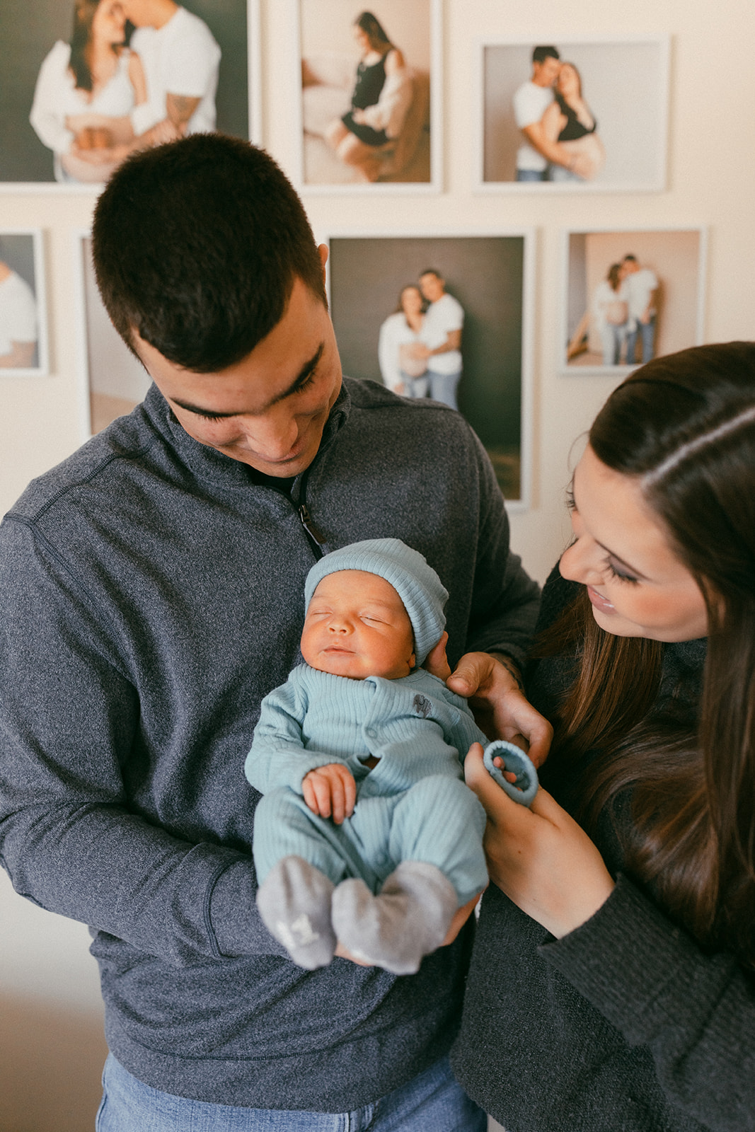 couple holding baby in nursery with gallery wall in the background during in-home newborn family photo session. 
