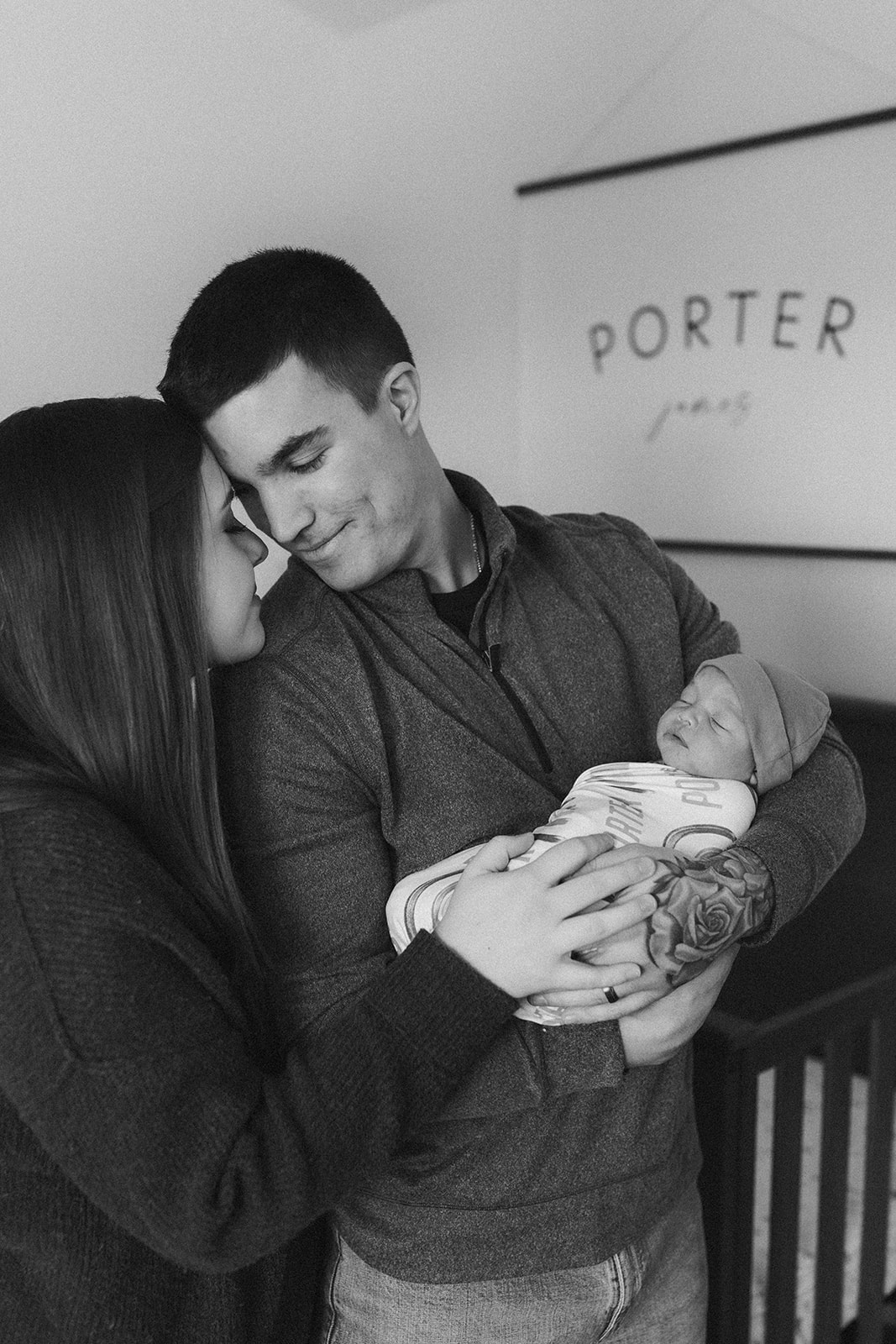 couple holding baby in nursery with name sign in background during in-home newborn family photo session. 