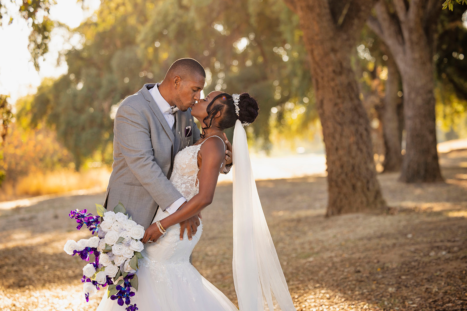 a husband kissing his wife at their post wedding couples portrait session at the pavilion at haggin oaks near trees