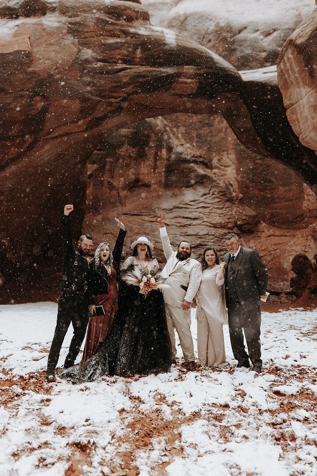 A wedding party cheering in the snow at Sand Dune Arch in Arches National Park.