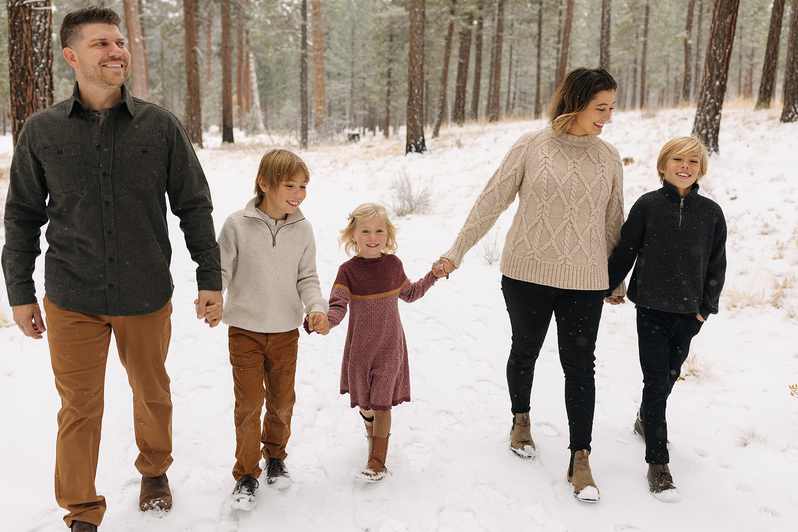 Family of 5 walking in a snowy setting at Shevlin Park in Bend, Oregon forming a straight line and laughing at each oth