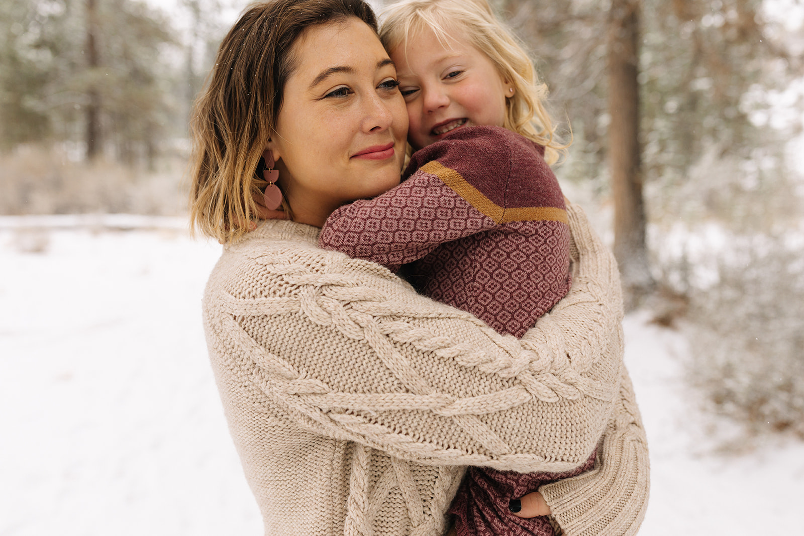 A mom and her young daughter embracing in a hug without looking at the camera in a snowy setting
