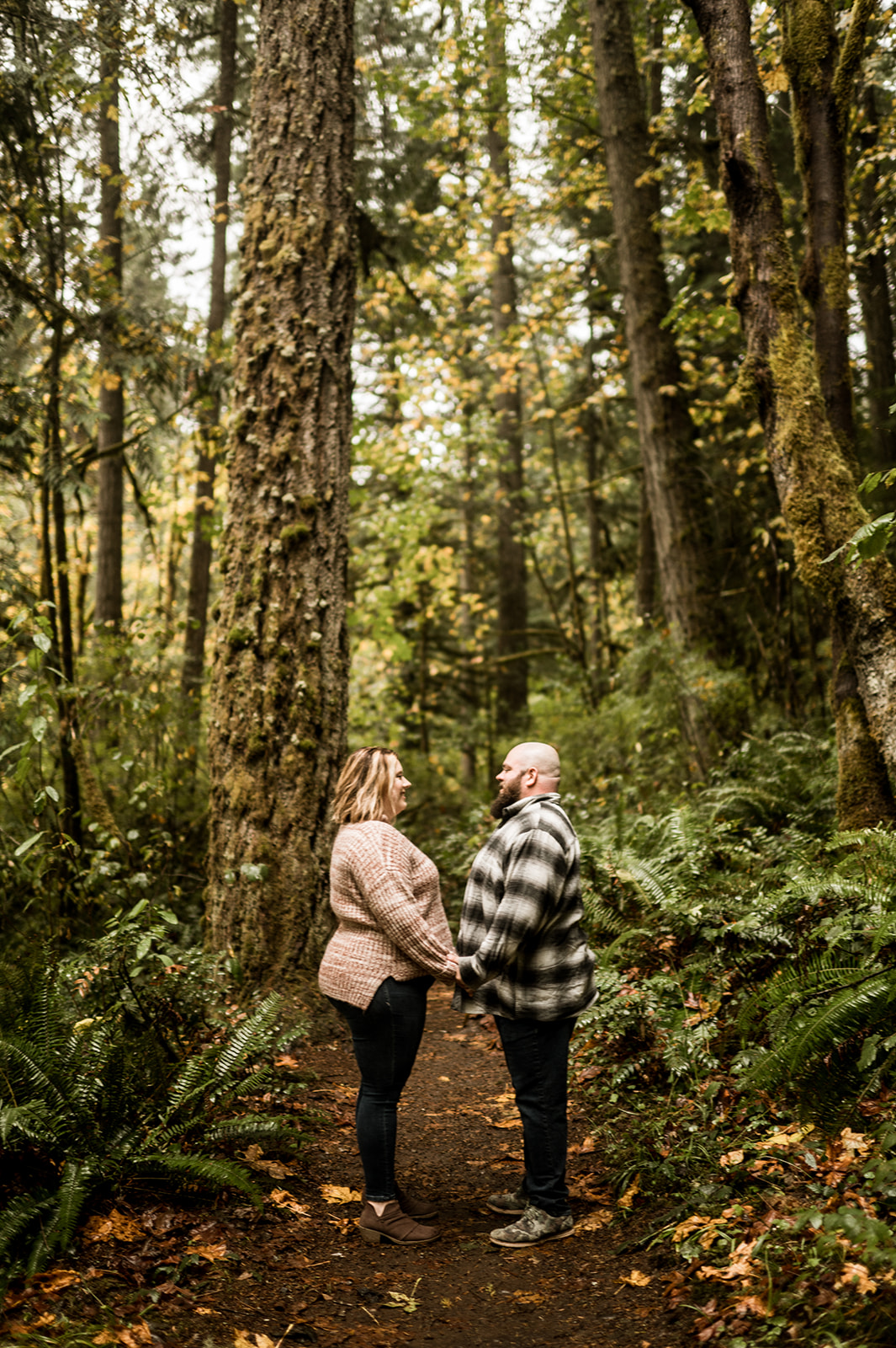 oregon couple stand in forest facing each other and holding hands for their engagement session