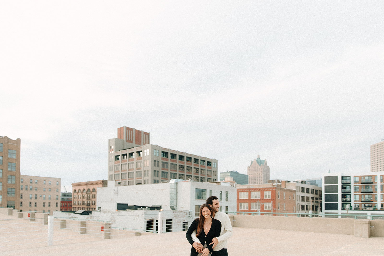 A couple poses on a third ward rooftop with the Milwaukee city skyline in the background before their proposal