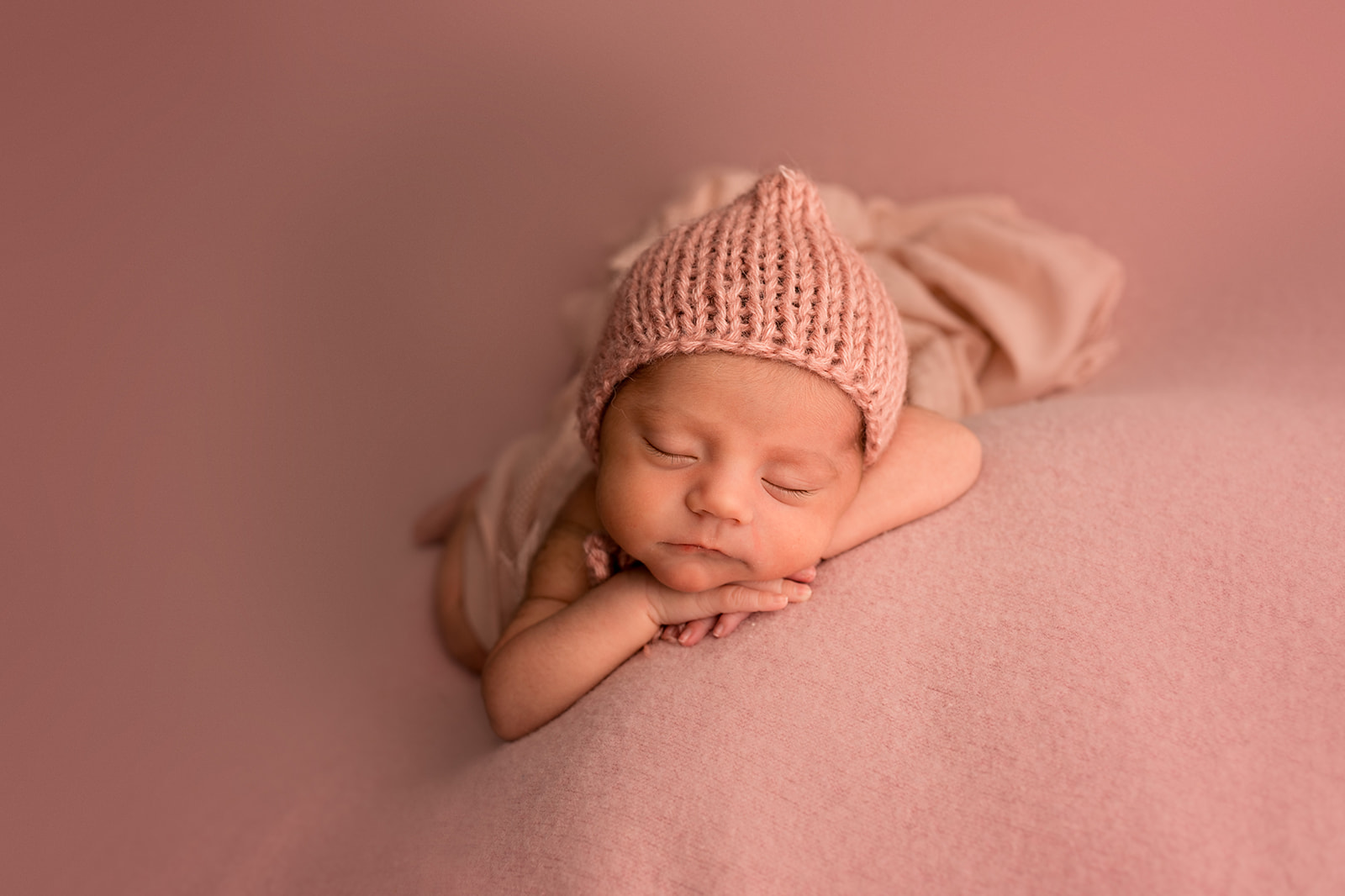 Baby girl posed with head on hands in a pink hat with a pink backdrop