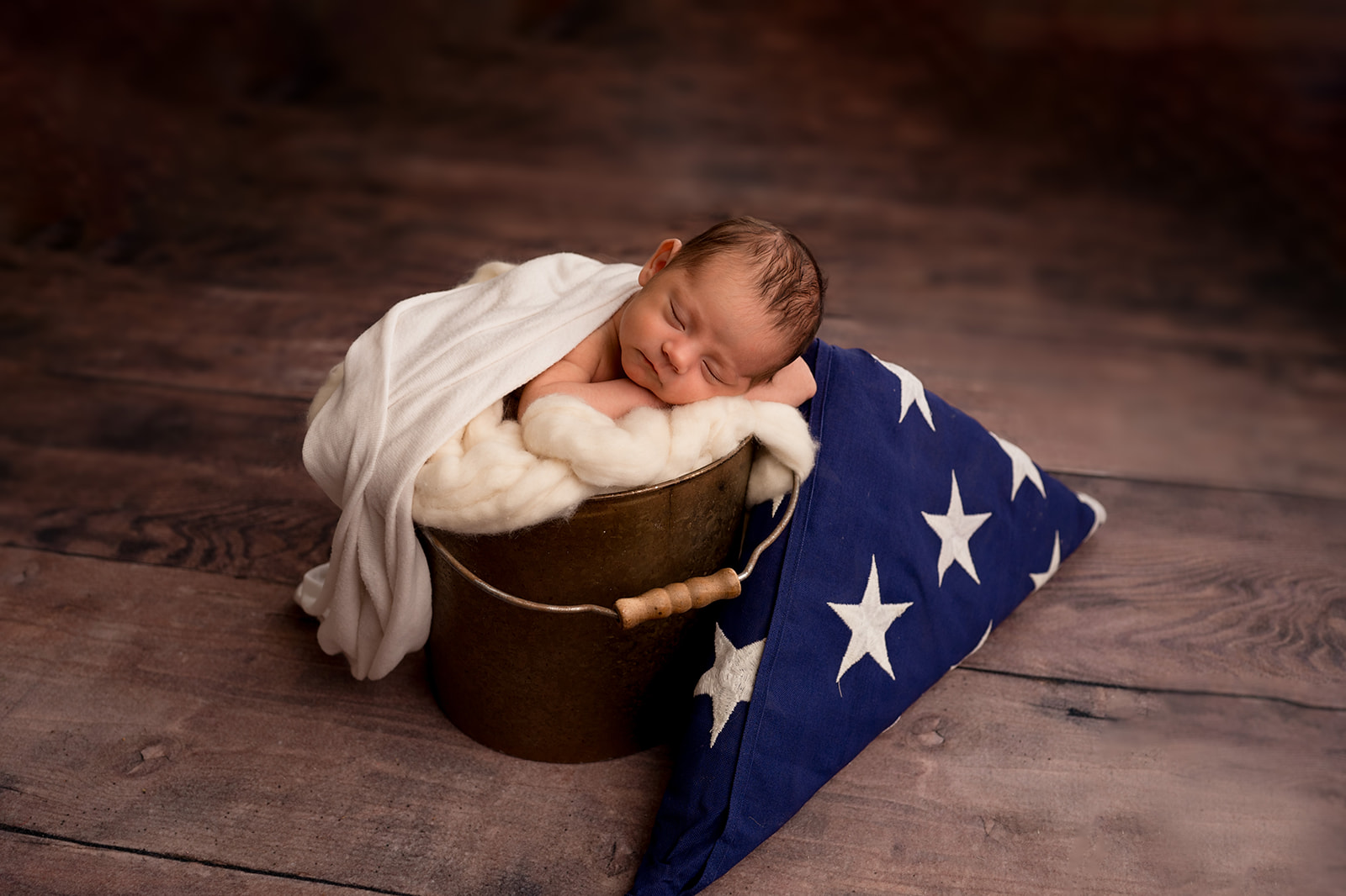 Newborn baby girl in a bucket on a wooden floor with folded american flag