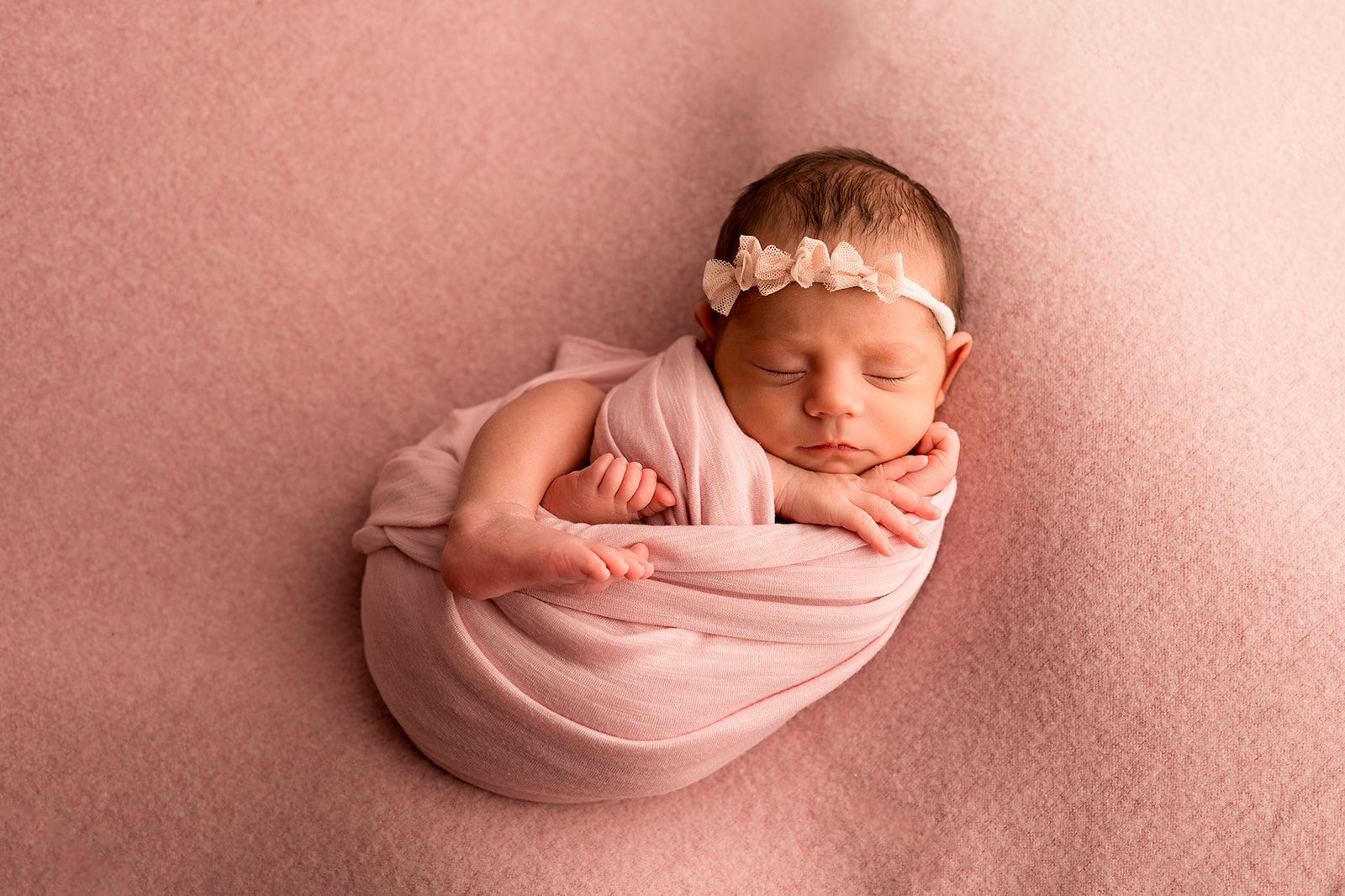 Newborn baby girl swaddled in pink on a pink backdrop with her tiny toes and fingers poking out for studio portraits