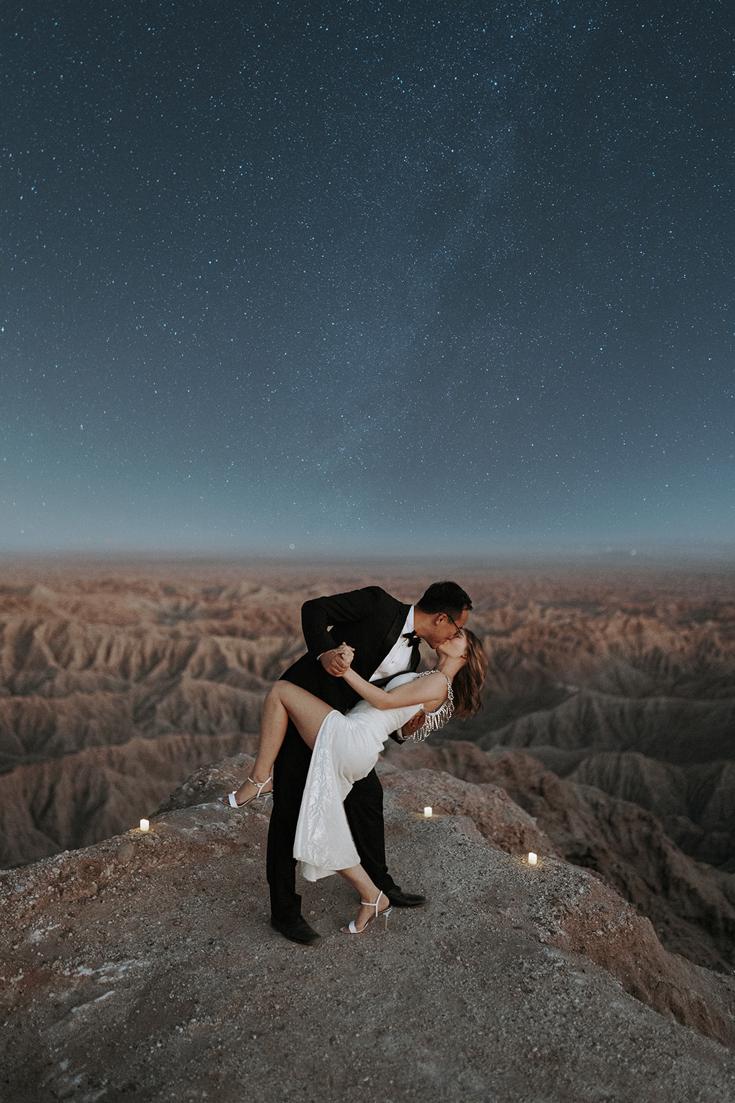 An eloping couple kissing on a cliff over a canyon in Anza Borrego under the Milky Way.