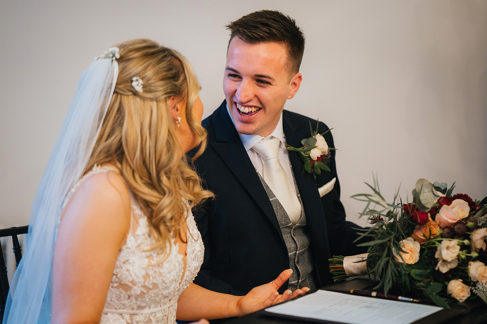 the groom laughs at his new wife as she signs the wedding register