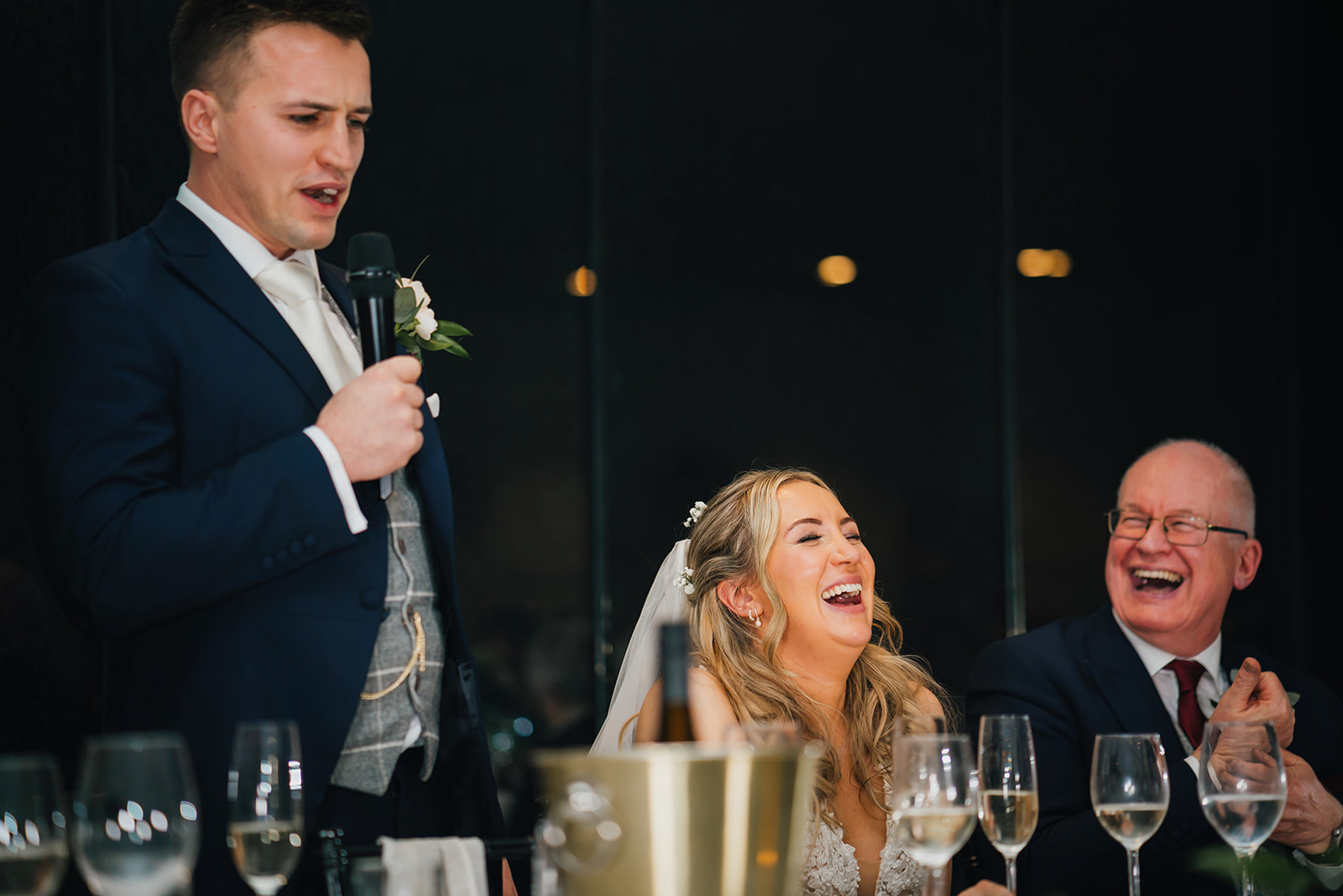 the groom delivers his speech as the bride laughs