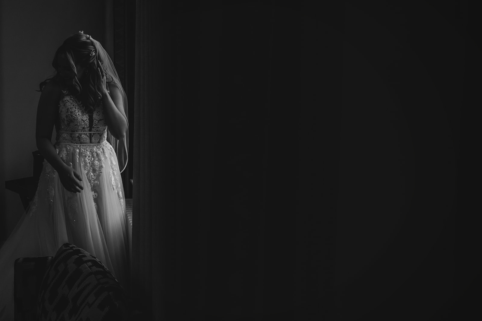 a black and white portrait of a bride in the window light. The rest of the frame is in shadow as a beam of light hits th