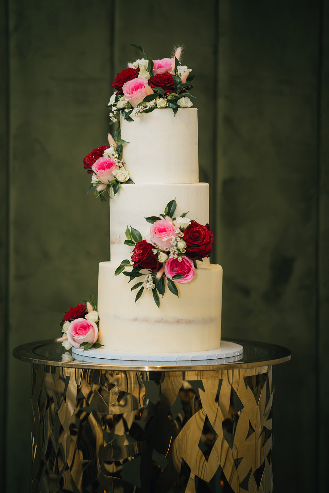 three tiered wedding cake with roses and other wedding flowers